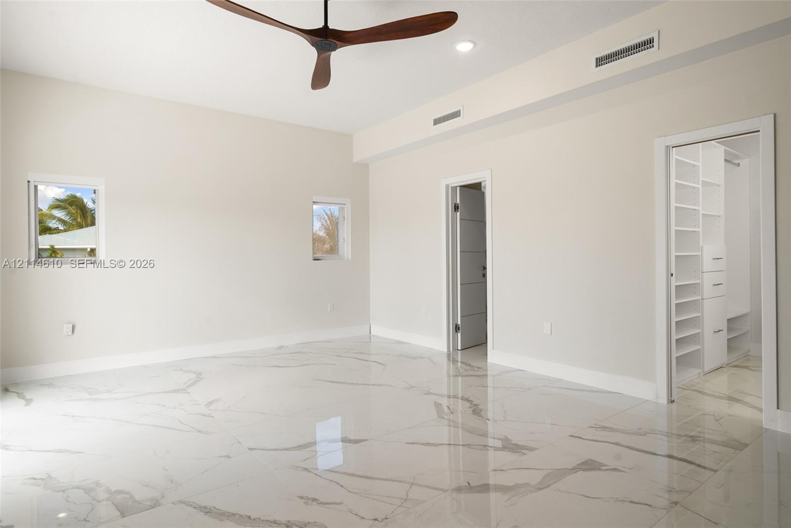 Polished stone-finish flooring featuring large-format veining, high ceilings, ceiling fan with aerodynamic blades, recessed lighting, and built-in walk-in closet shelving