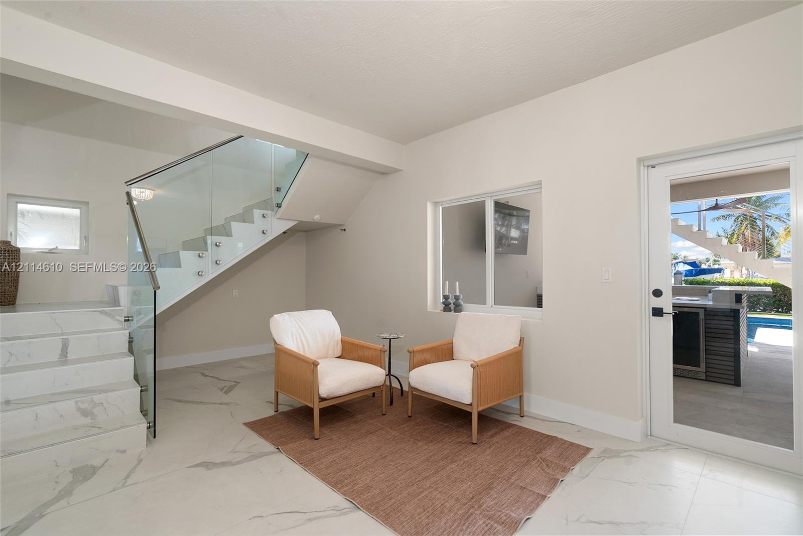Large-format stone flooring, staircase with glass railing and stainless steel standoffs, and full-glass exterior door