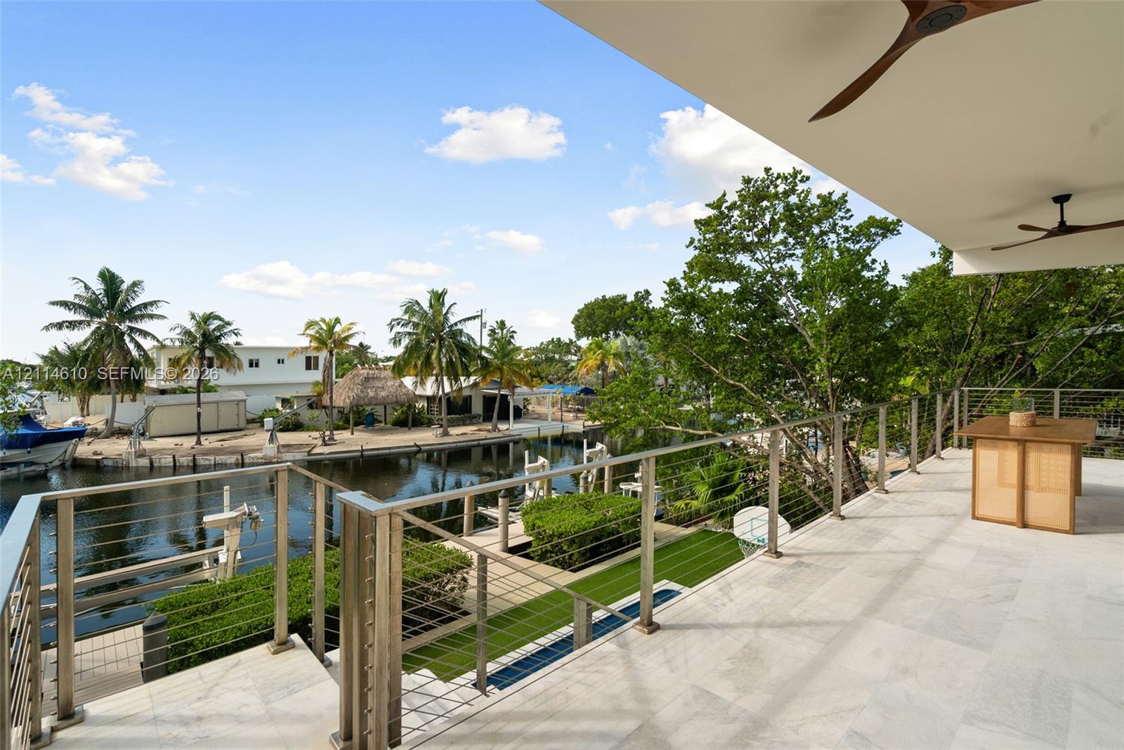 Covered balcony featuring stone flooring, stainless steel railing with cable infill, and ceiling-mounted fans