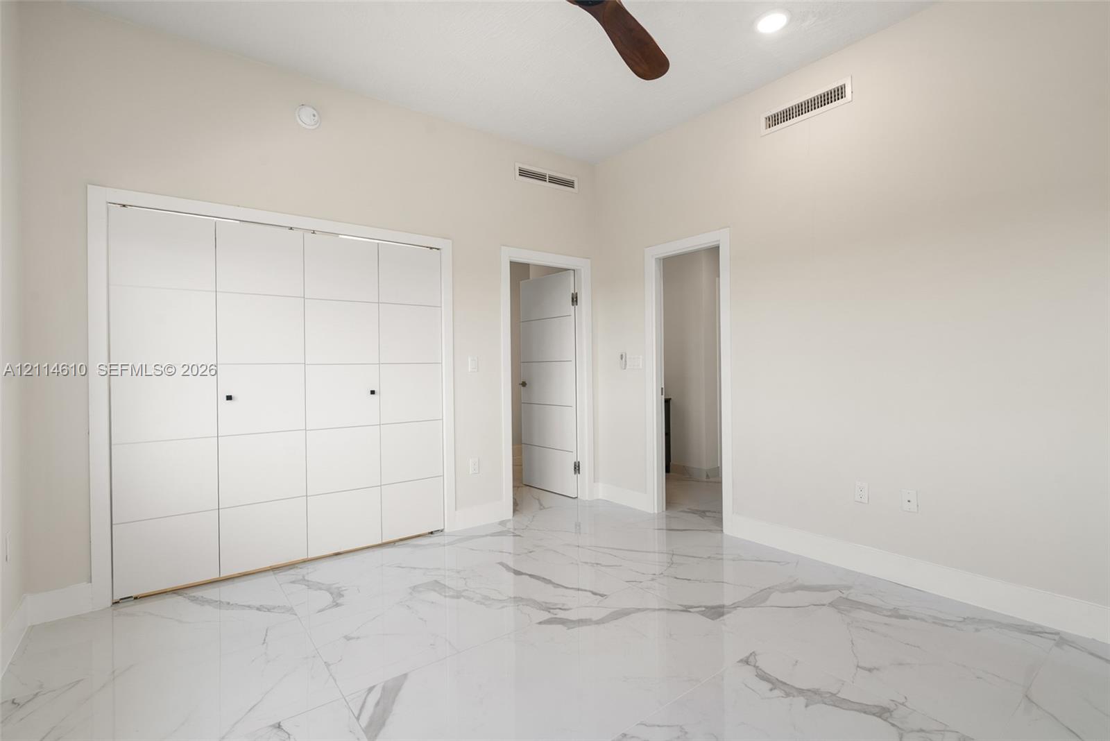 Room featuring large-format tile flooring with a veined finish, high ceilings, recessed lighting, a ceiling fan, and built-in closet cabinetry with panel detail