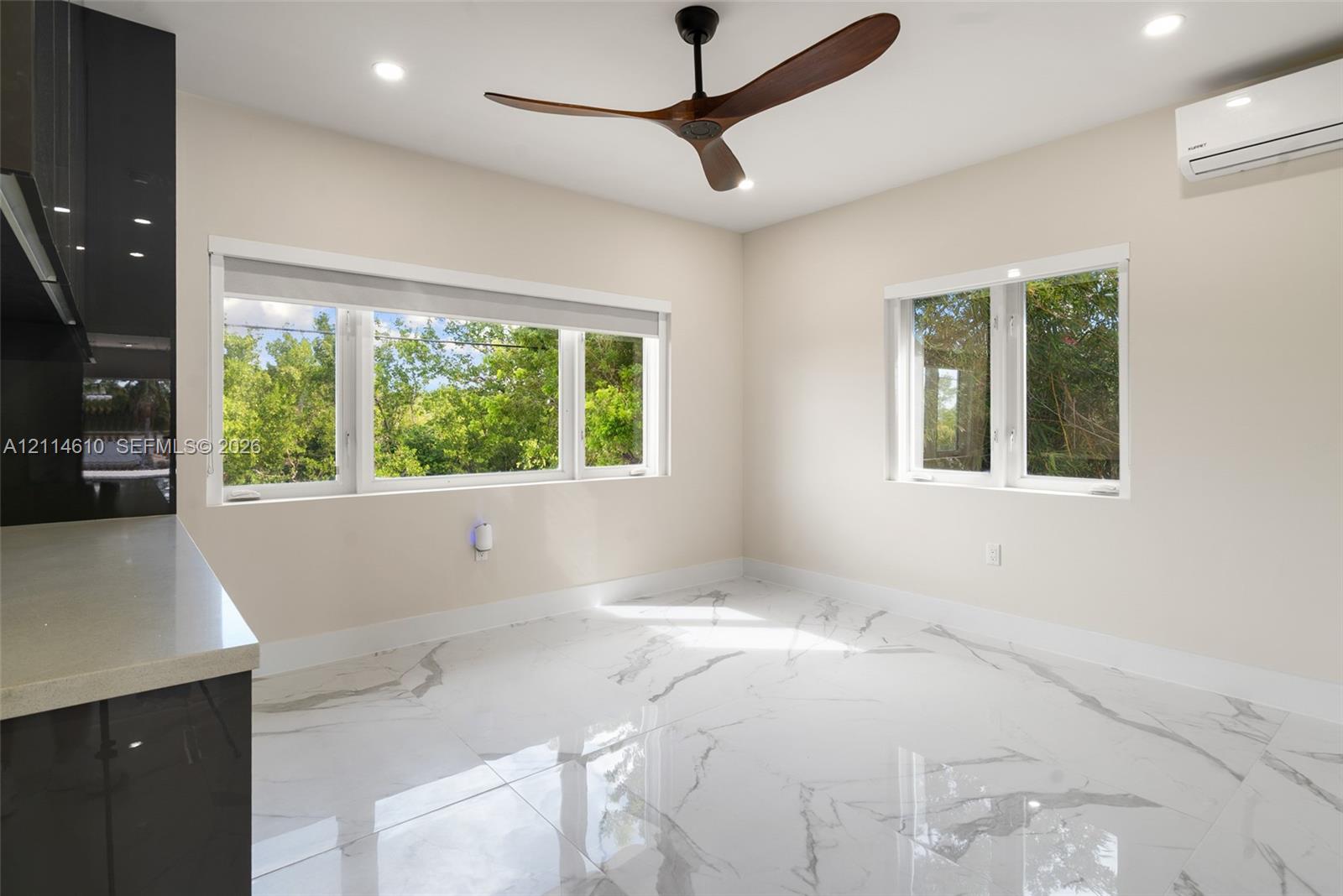 Polished tile flooring with veining, three-blade ceiling fan, recessed lighting, wall-mounted air conditioning unit, and large windows with greenery exposure