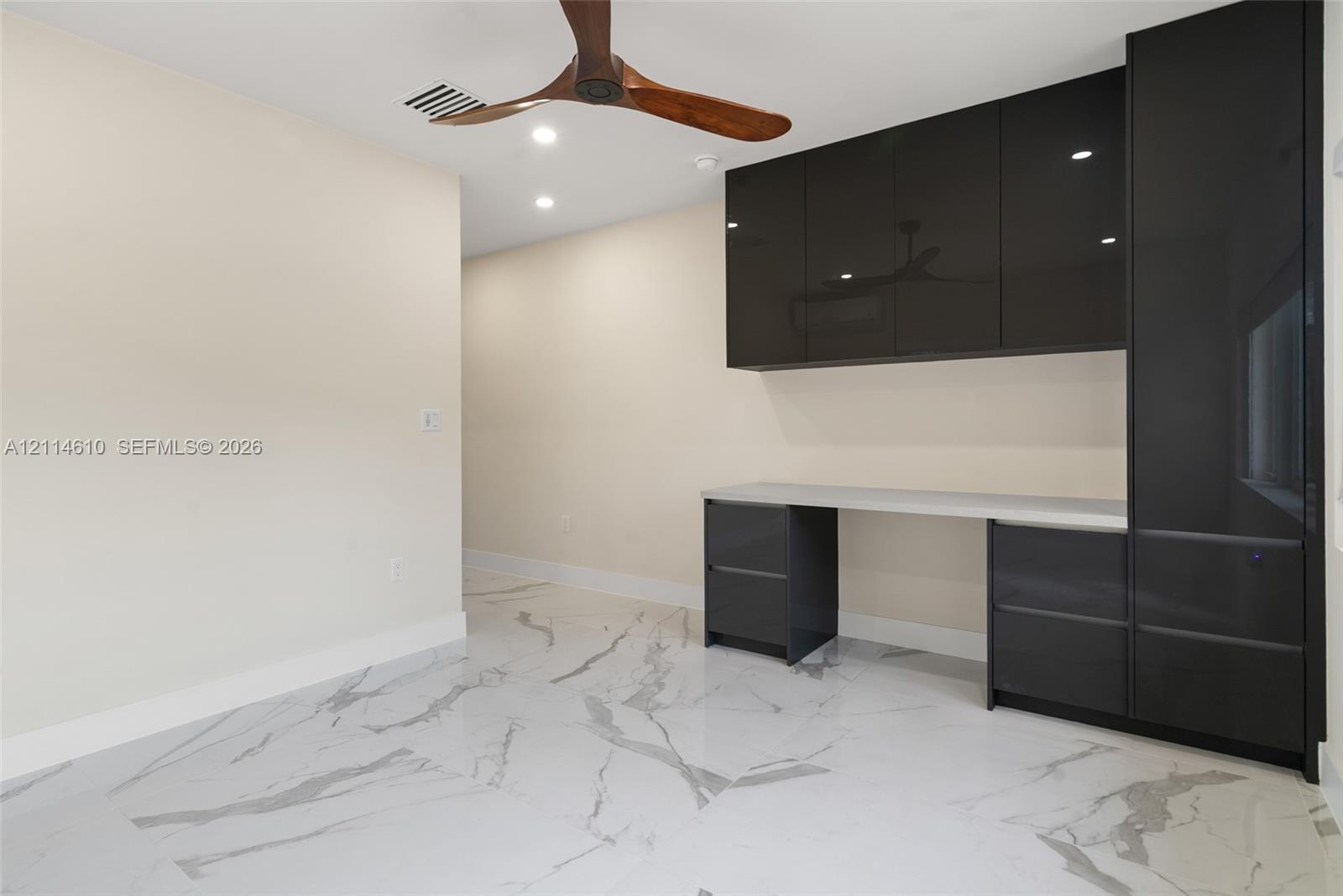 Built-in cabinetry with high-gloss dark finish, solid surface countertop, large-format tile flooring with marble-finish veining, and wooden-blade ceiling fan