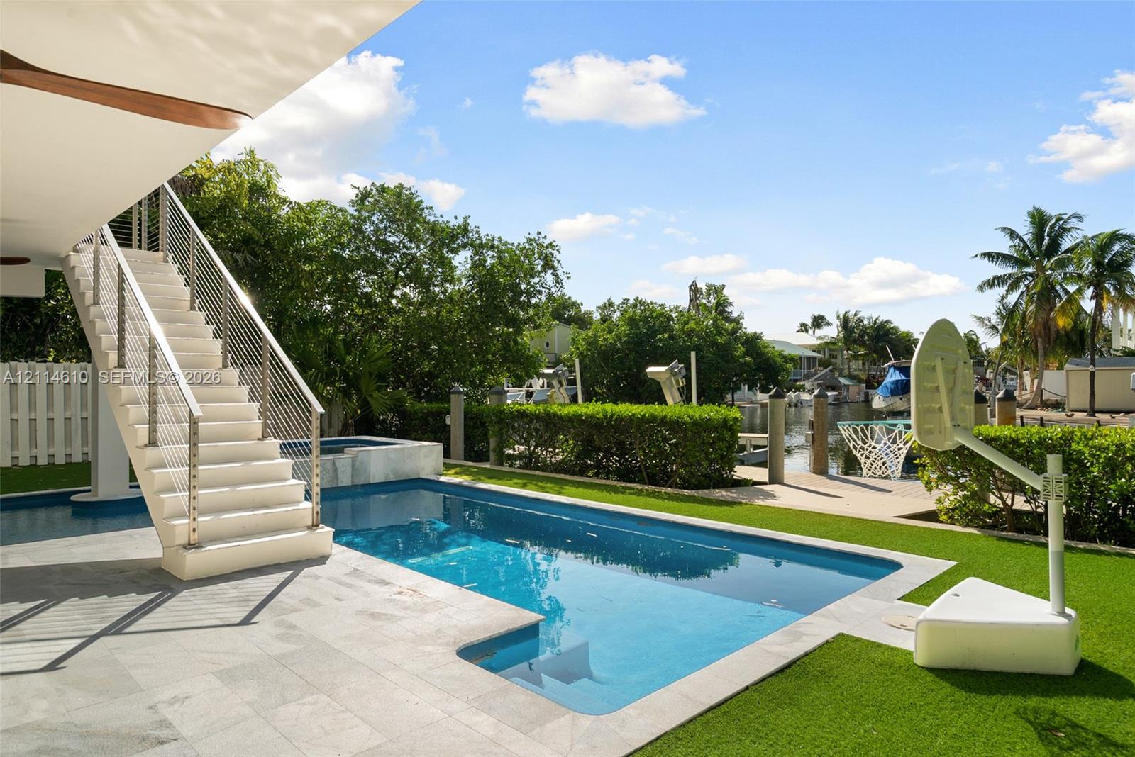 Outdoor living space featuring an in-ground swimming pool, stone-paver decking, elevated staircase with stainless steel cable railing, and direct water frontage with private boat slips