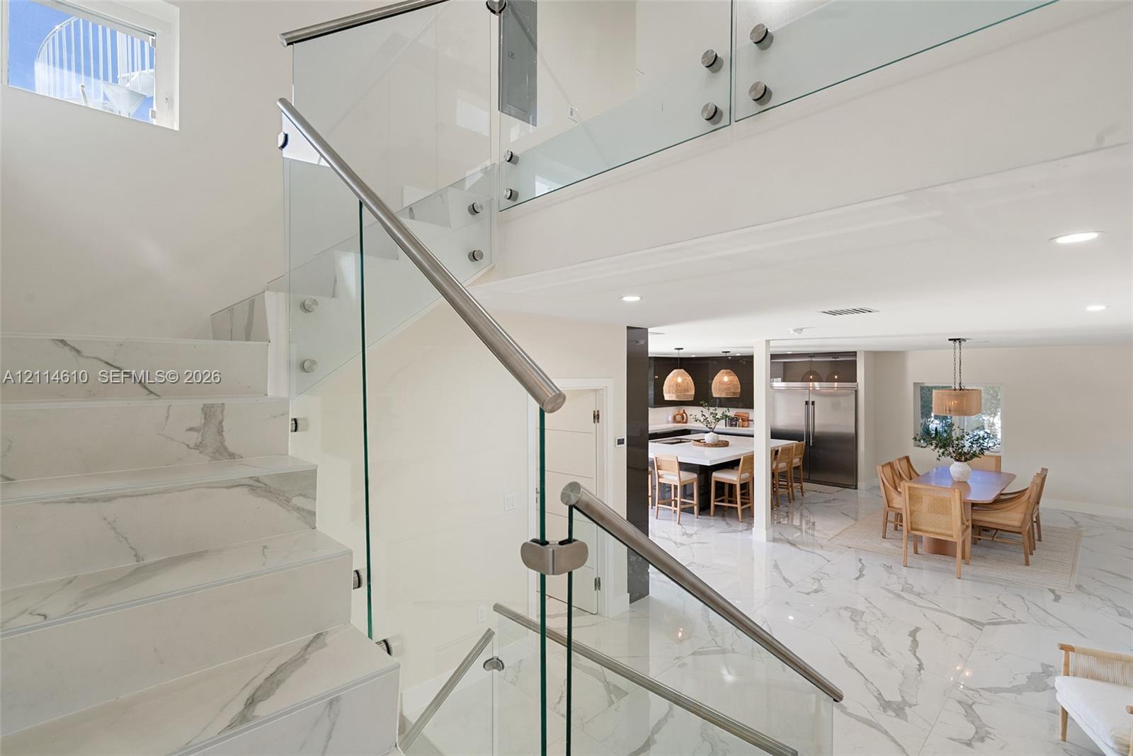 Staircase featuring stone-finish treads and risers, a glass railing system with metal standoffs, and large-format stone-finish flooring throughout