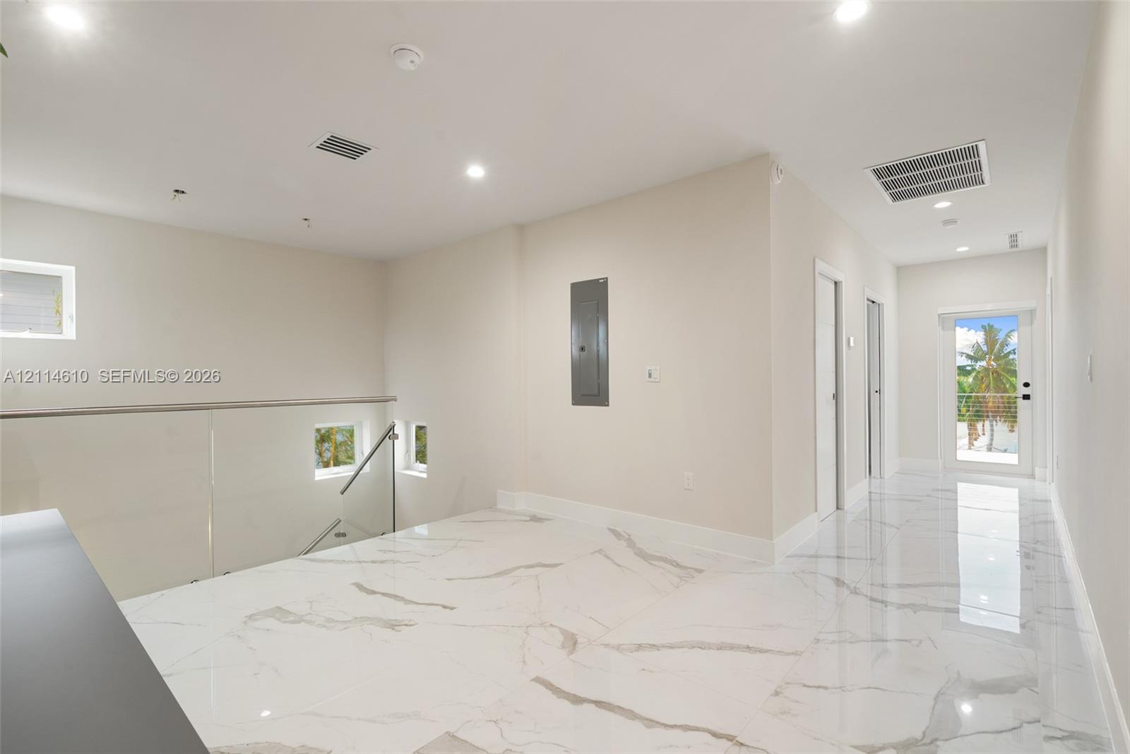 Large-format white tile flooring with grey veining, recessed lighting, and a glass panel railing with a metallic handrail