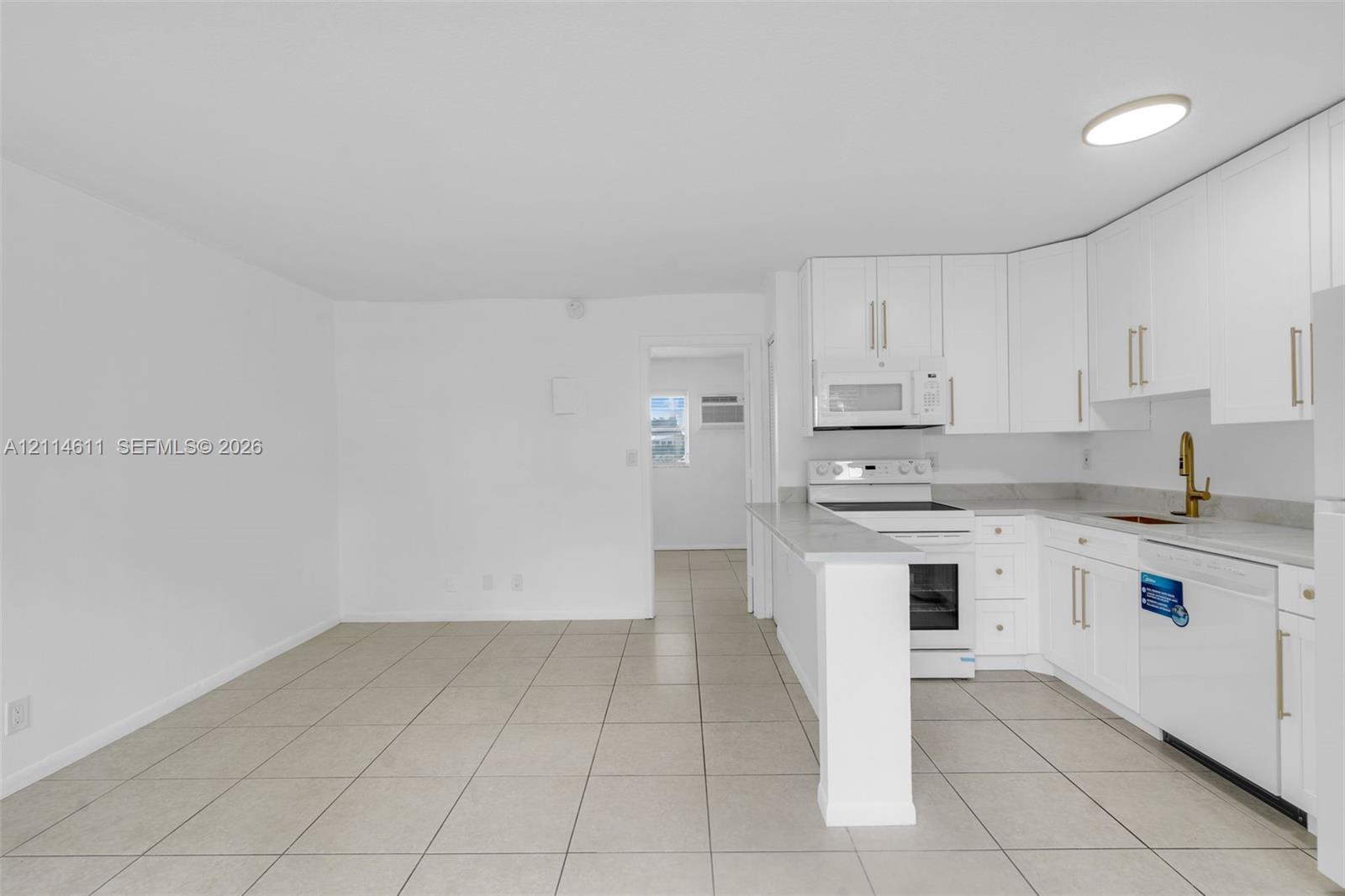 Kitchen featuring white shaker-style cabinetry, a gold-tone faucet, tiled flooring, and a peninsula counter Kitchen featuring white shaker-style cabinetry, a gold-tone faucet, tiled flooring, and a peninsula counter