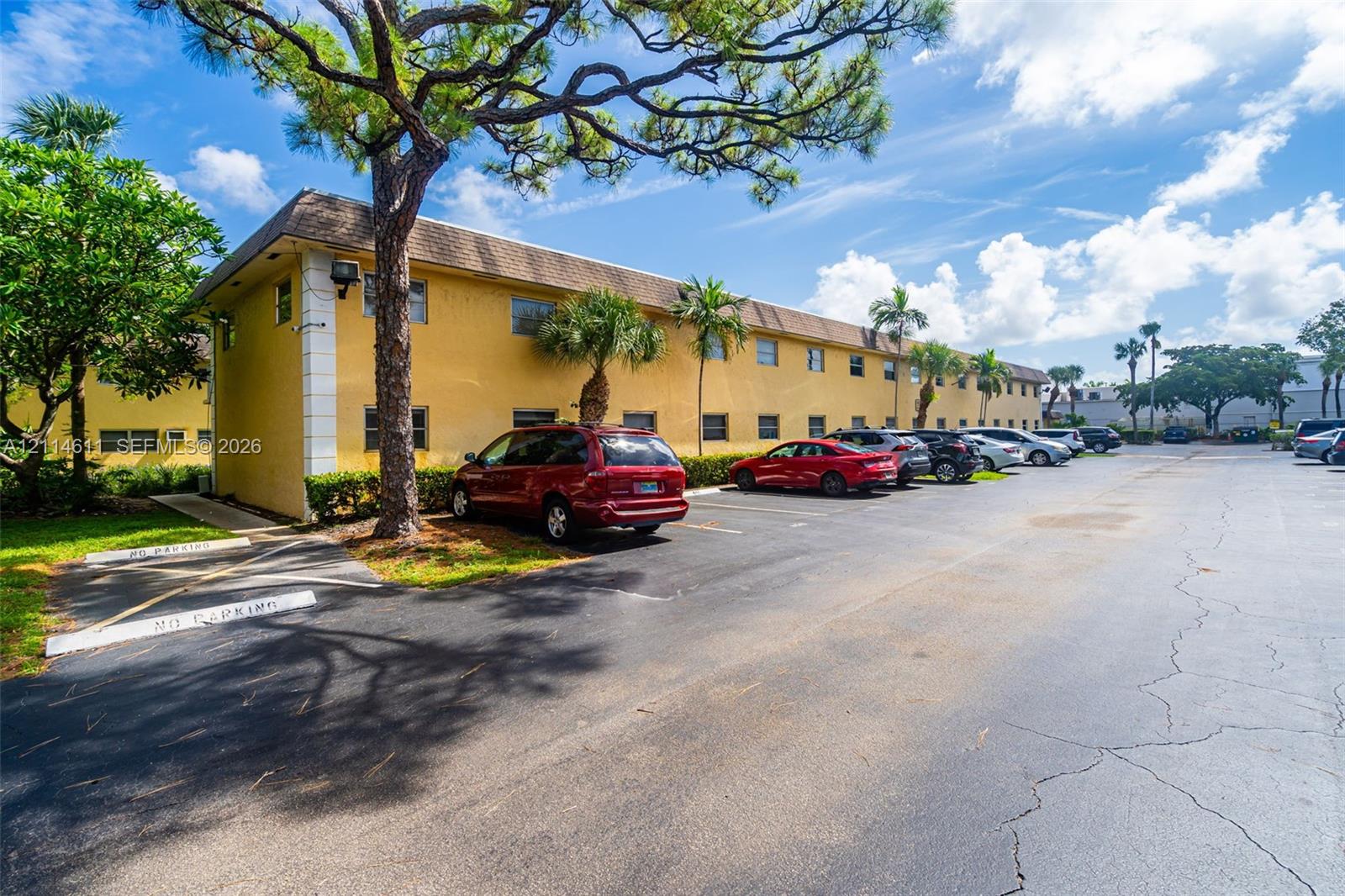 Multi-story exterior featuring a textured stucco facade, asphalt-paved surface parking, and mature perimeter landscaping