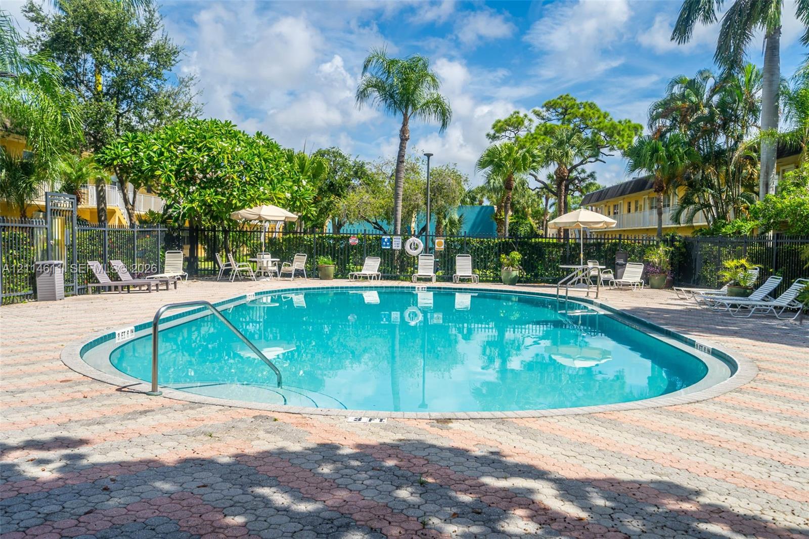 Swimming pool with integrated entry steps and stainless steel handrail, surrounded by decorative concrete paver decking, enclosed by perimeter metal fencing and mature landscaping