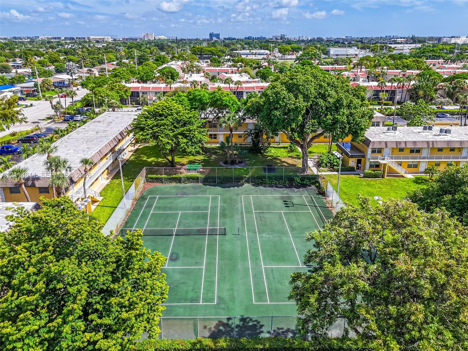 Outdoor tennis facility featuring dual courts enclosed by chain-link fencing and mature perimeter landscaping