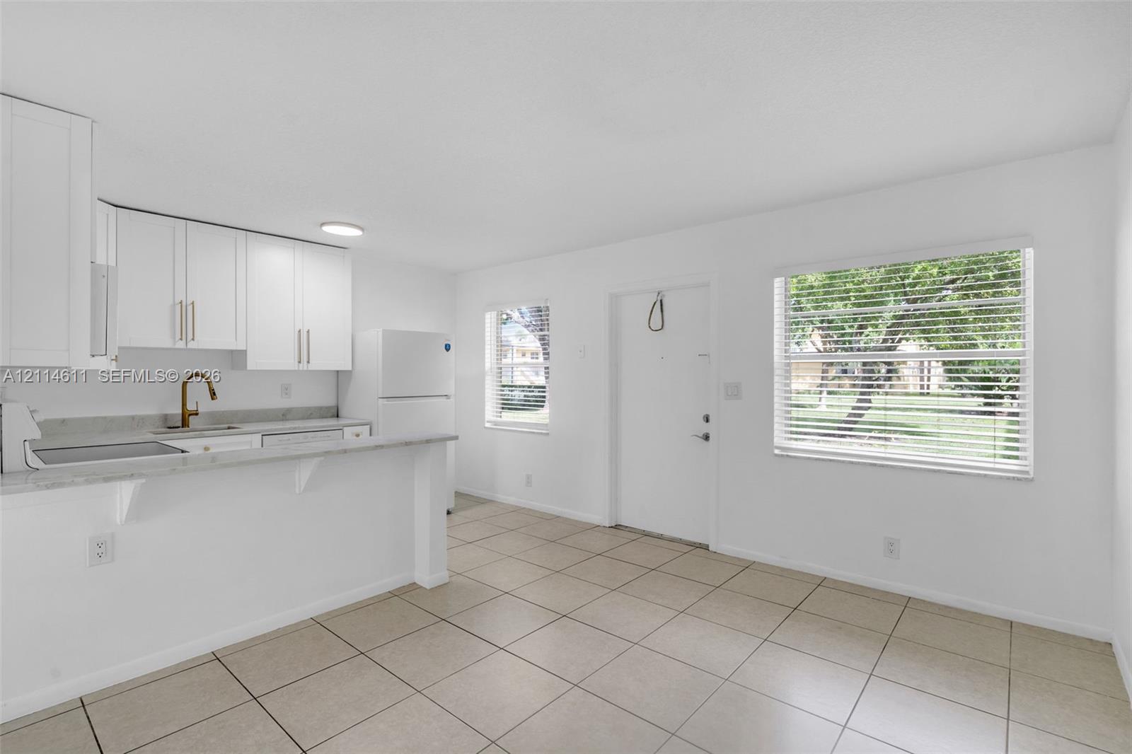 Kitchen featuring white cabinetry, stone-finish countertops, an under-mount sink with a bronze-tone faucet, and tile flooring Kitchen featuring white cabinetry, stone-finish countertops, an under-mount sink with a bronze-tone faucet, and tile flooring