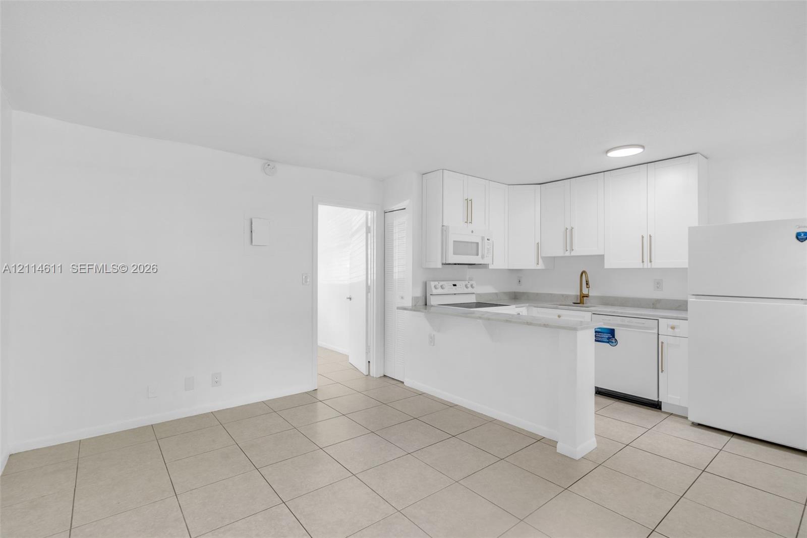 Kitchen featuring white cabinetry, solid-surface countertops, tile flooring, integrated appliances, and a brass-finish faucet Kitchen featuring white cabinetry, solid-surface countertops, tile flooring, integrated appliances, and a brass-finish faucet