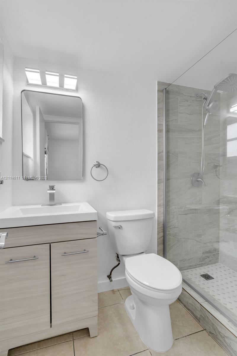 Bathroom featuring a wood-finish vanity with a rectangular integrated sink, wall-mounted rectangular mirror, three-light fixture, and a glass-enclosed shower with stone-tile surround and a handheld showerhead