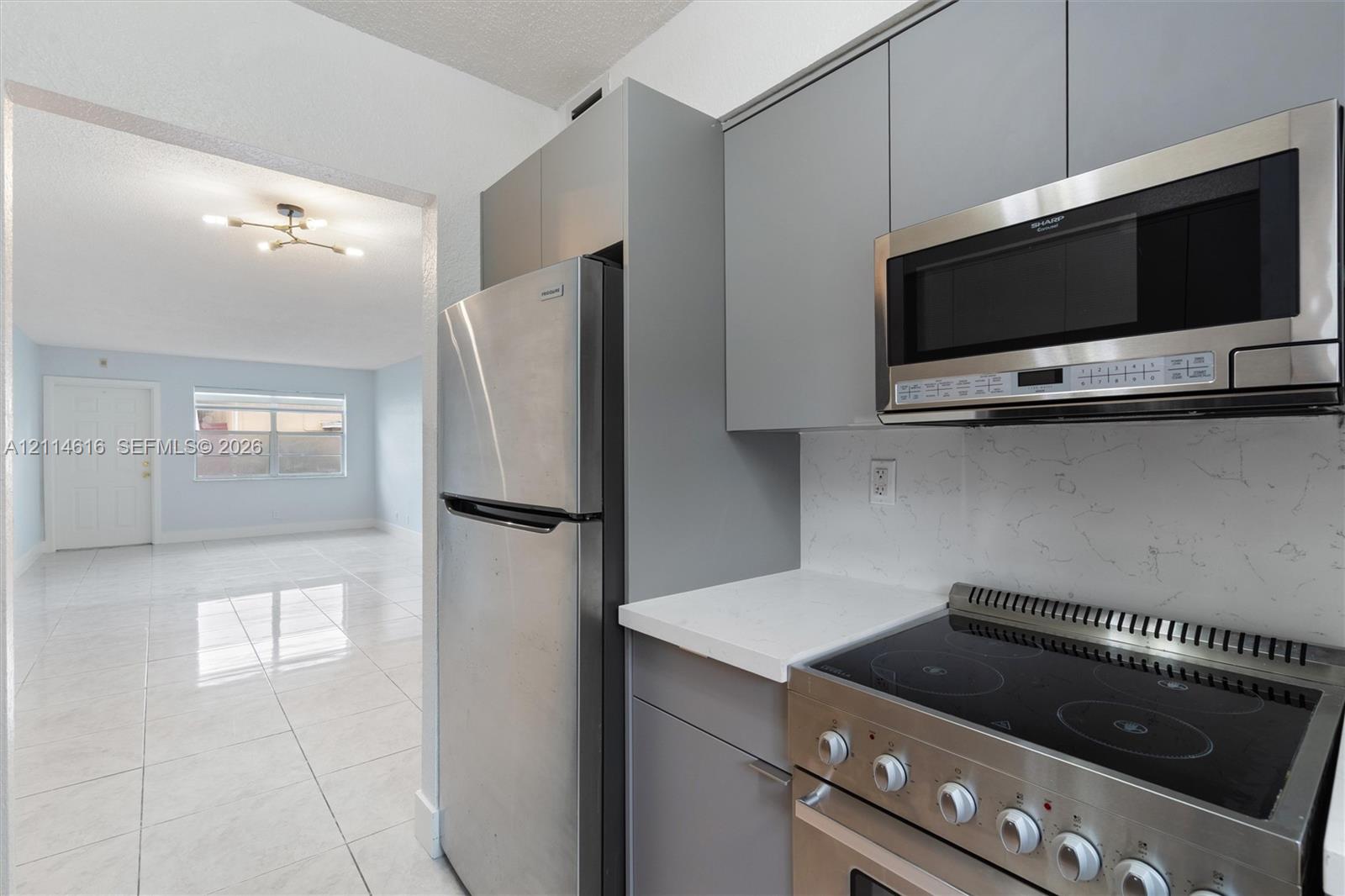 Kitchen featuring grey flat-panel cabinetry, stainless steel appliances, stone-look countertops, and high-gloss tile flooring
