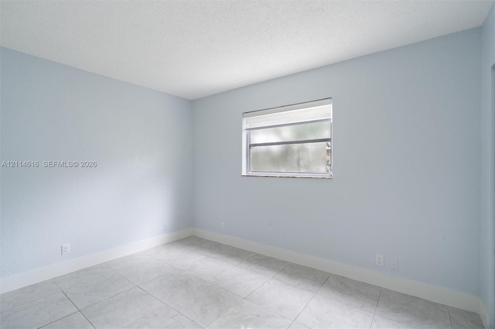 Interior room featuring large-format ceramic tile flooring, neutral wall paint, and a single-hung window with a roller shade
