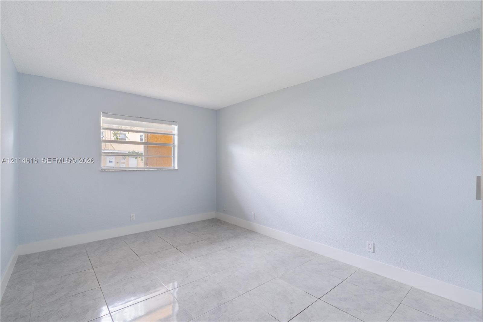 Neutral interior room featuring light-toned wall finishes, large-format tile flooring, and a horizontal louvered window