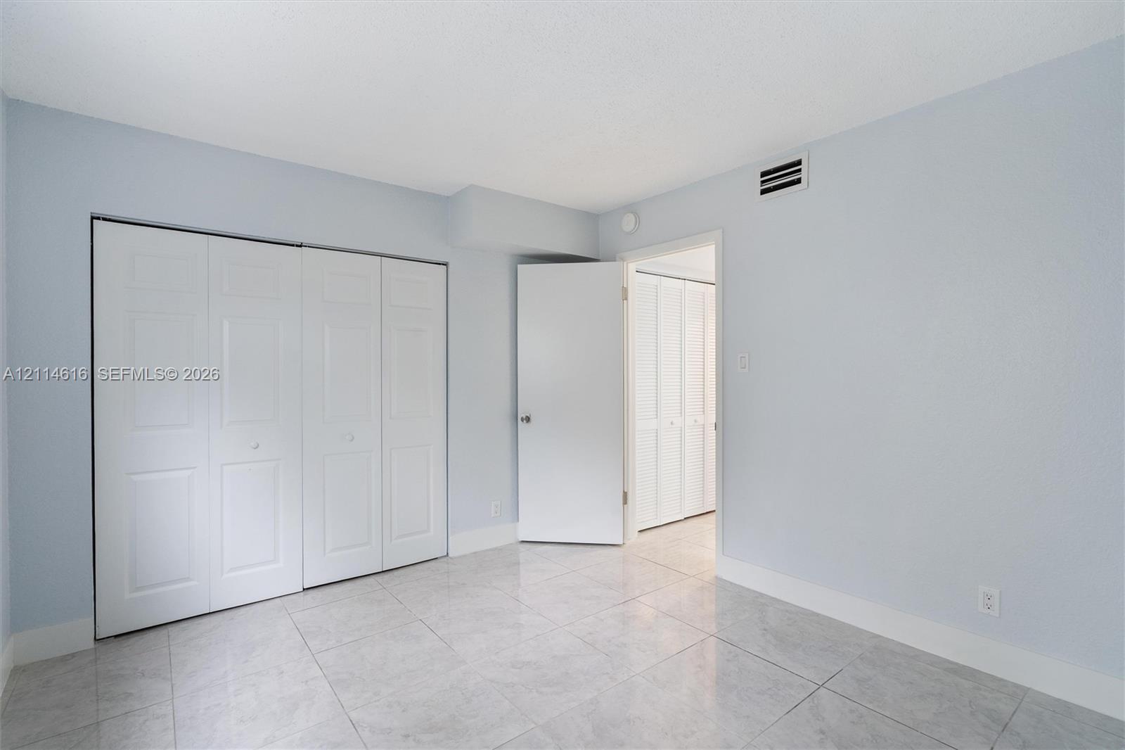 Interior space featuring neutral wall tones, large-format tile flooring, and integrated white bi-fold closet doors