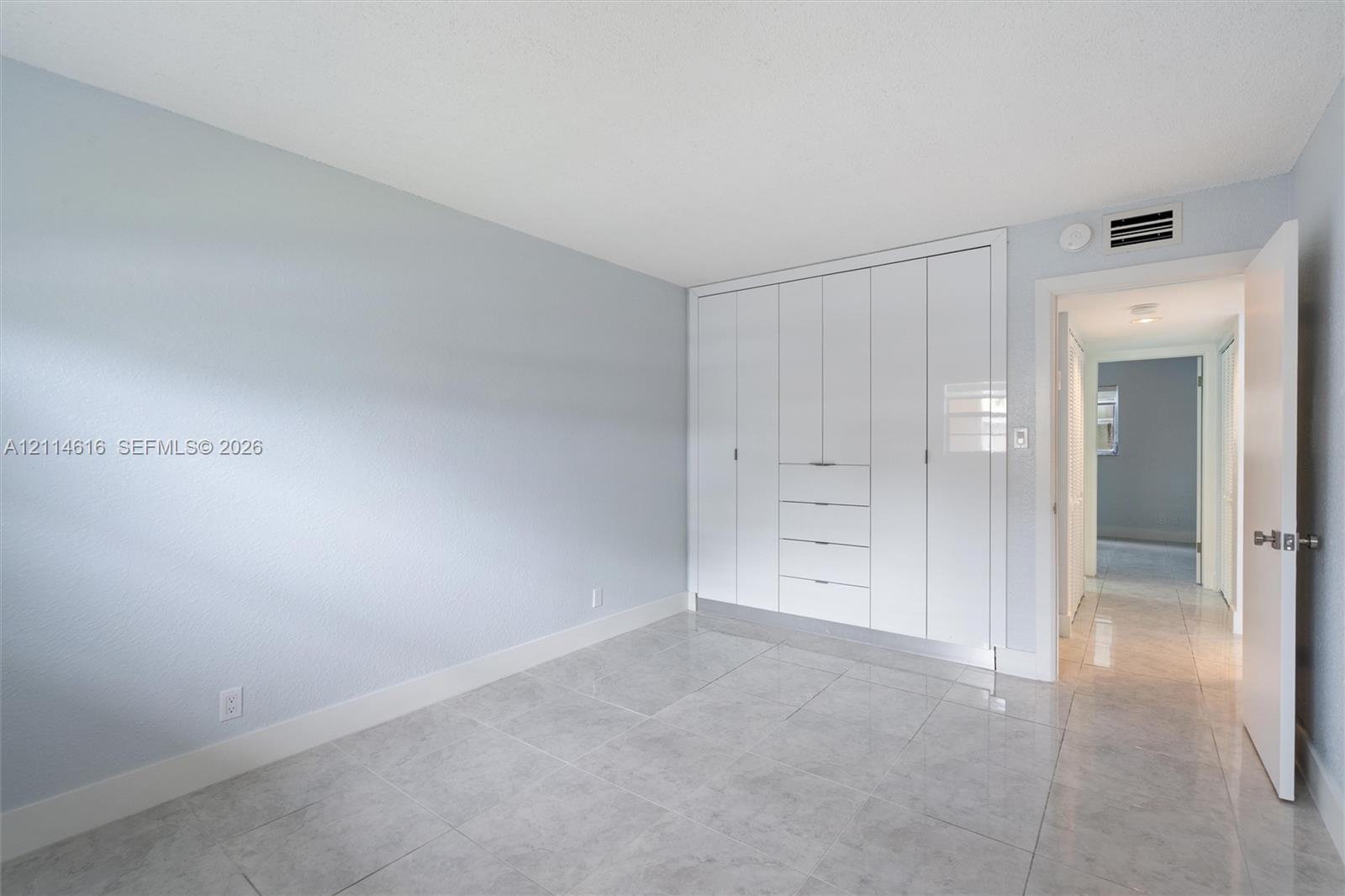 Neutral-toned room featuring large-format tile flooring and floor-to-ceiling built-in white cabinetry with integrated drawer storage