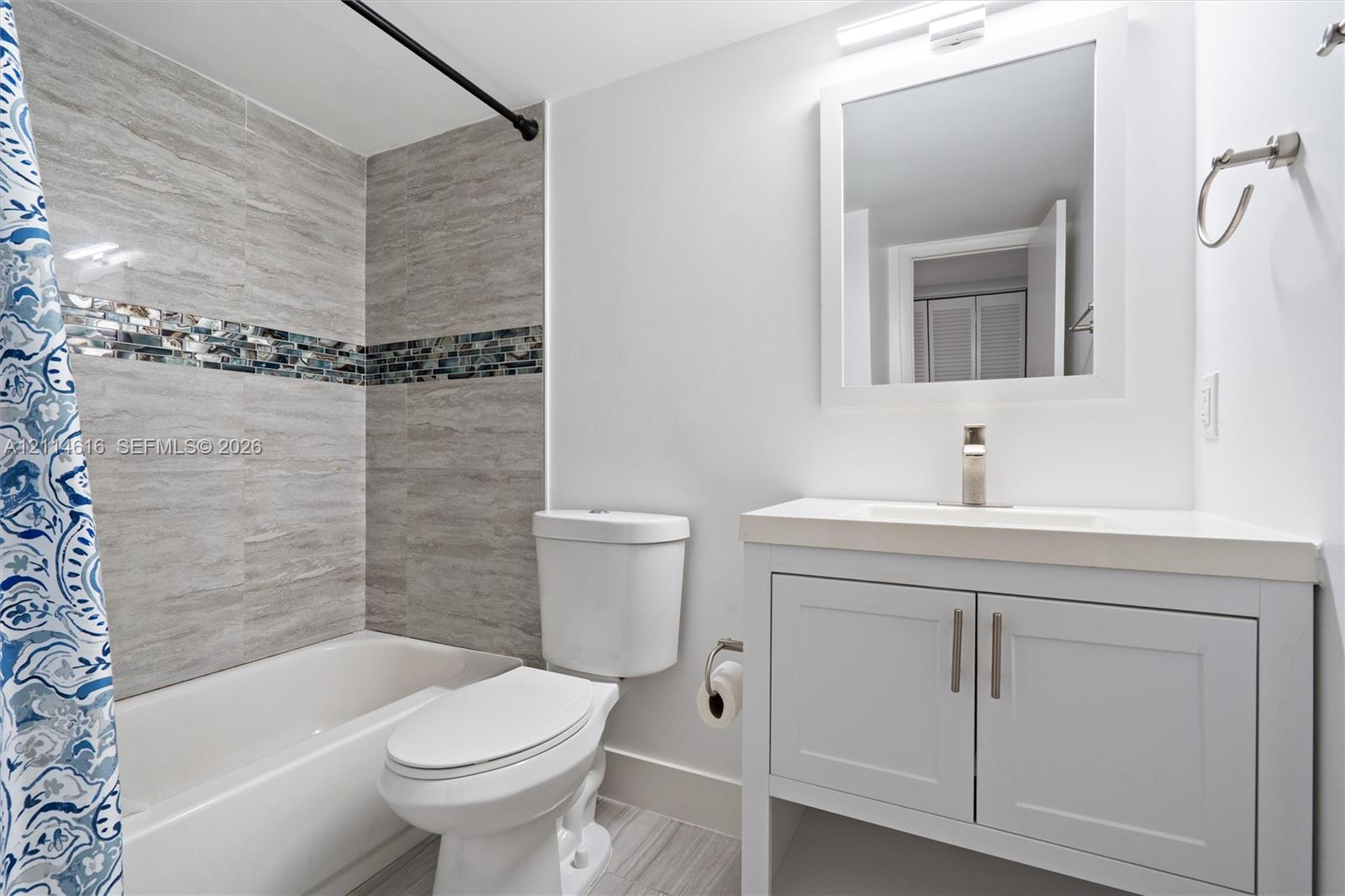 Bathroom featuring a vanity with shaker-style cabinetry and a single-basin countertop, a framed wall mirror, and a shower-tub combination accented with horizontal stone-finish tile and a decorative mosaic inlay