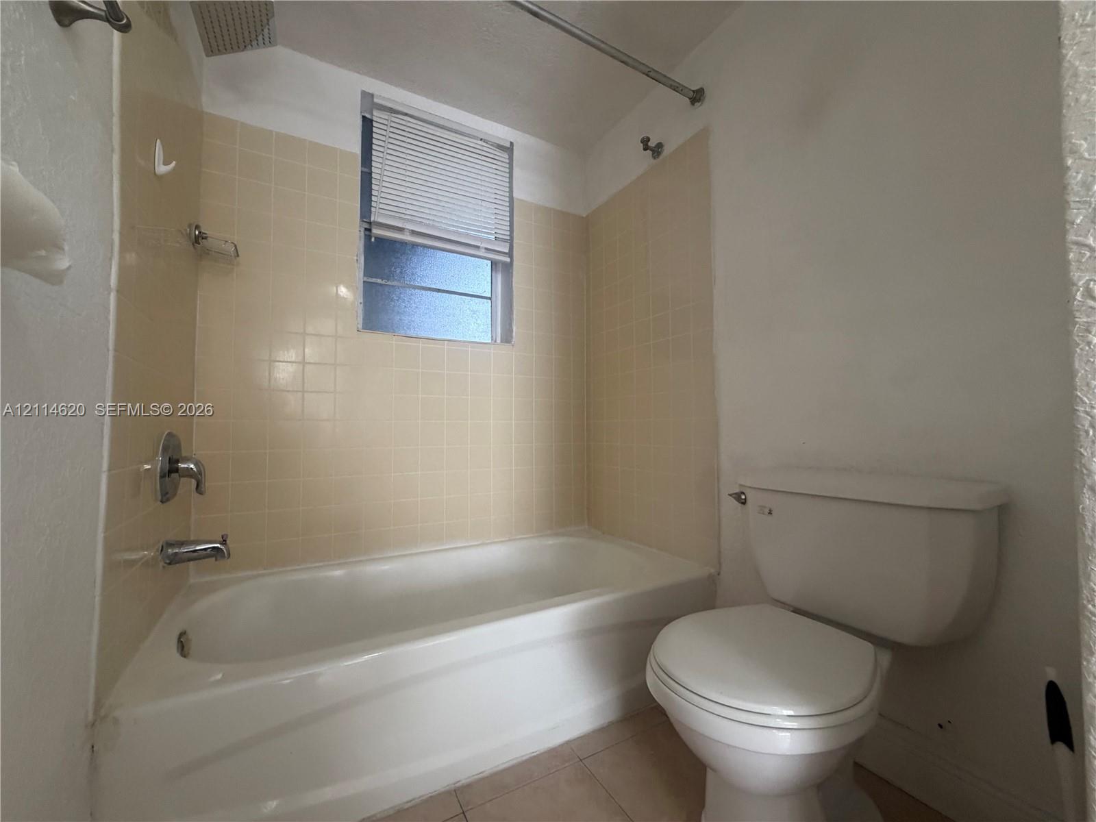 Bathroom featuring a porcelain tub, beige square-tile wall surround, chrome plumbing fixtures, and a window with integrated blinds