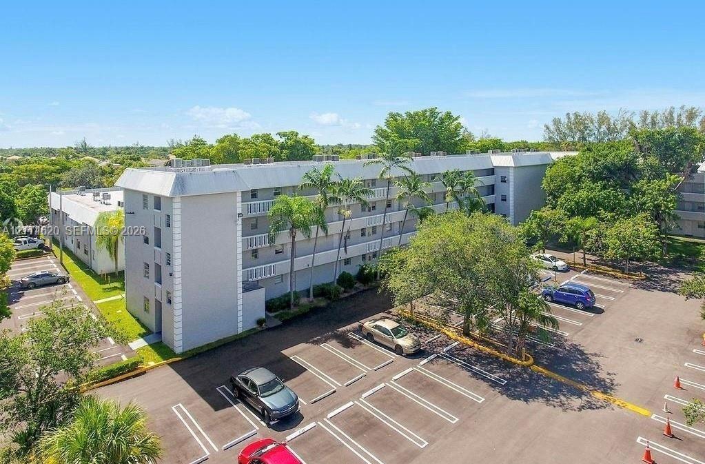 Multi-story residential building exterior featuring a light-toned stucco facade, open-air balcony corridors, and dedicated surface parking
