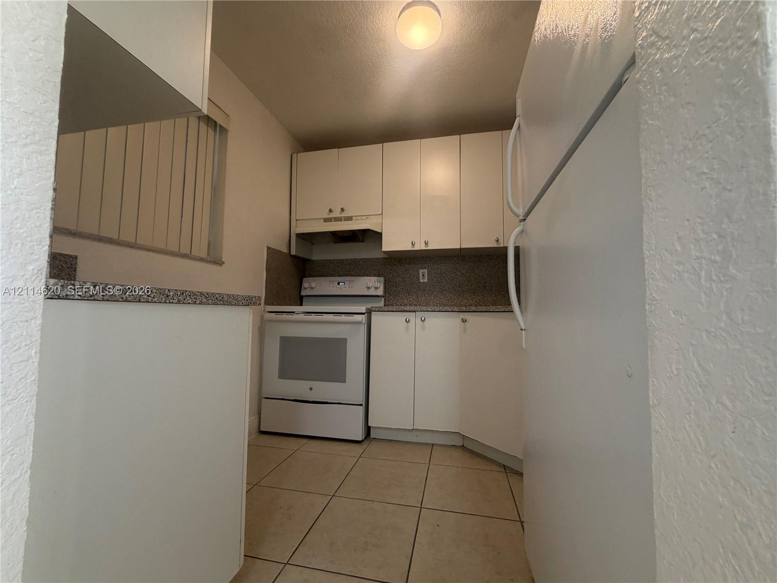 Kitchen featuring white cabinetry, solid-surface countertops, tile flooring, and white built-in appliances