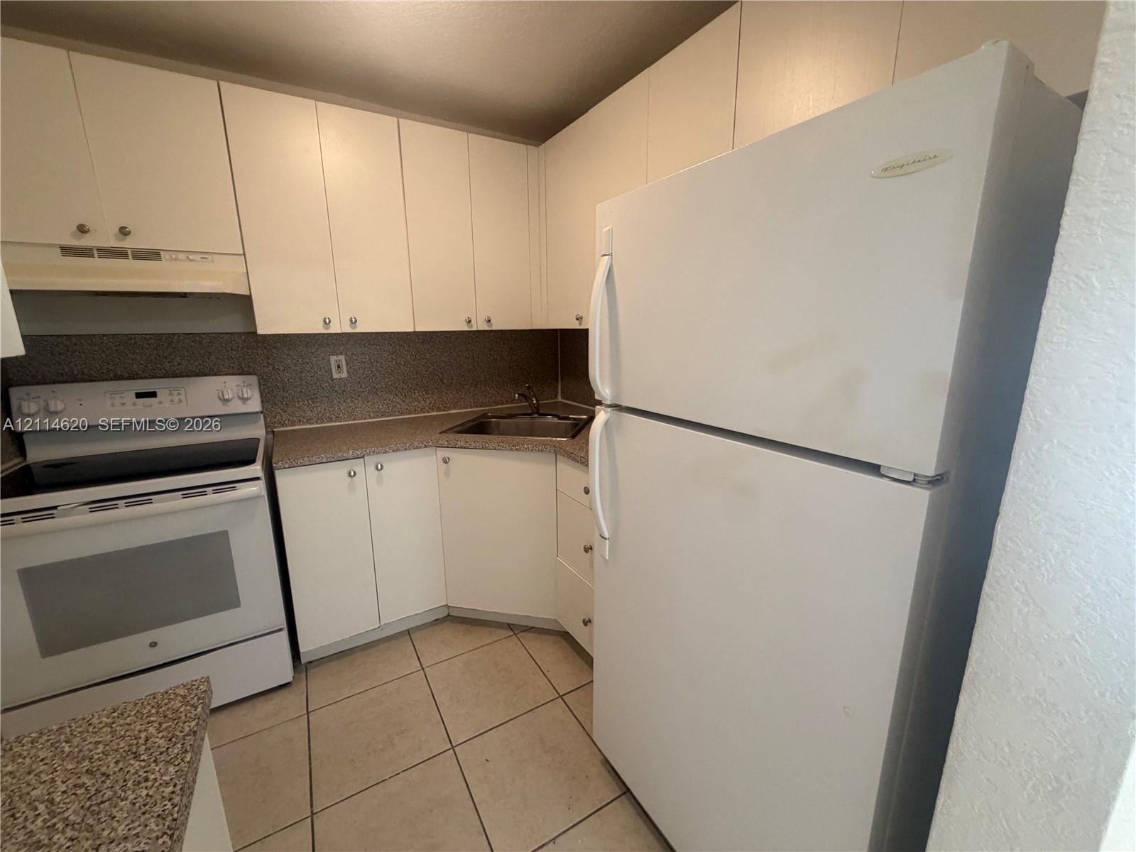 Kitchen featuring white cabinetry, solid-surface countertops, tile flooring, and white built-in appliances