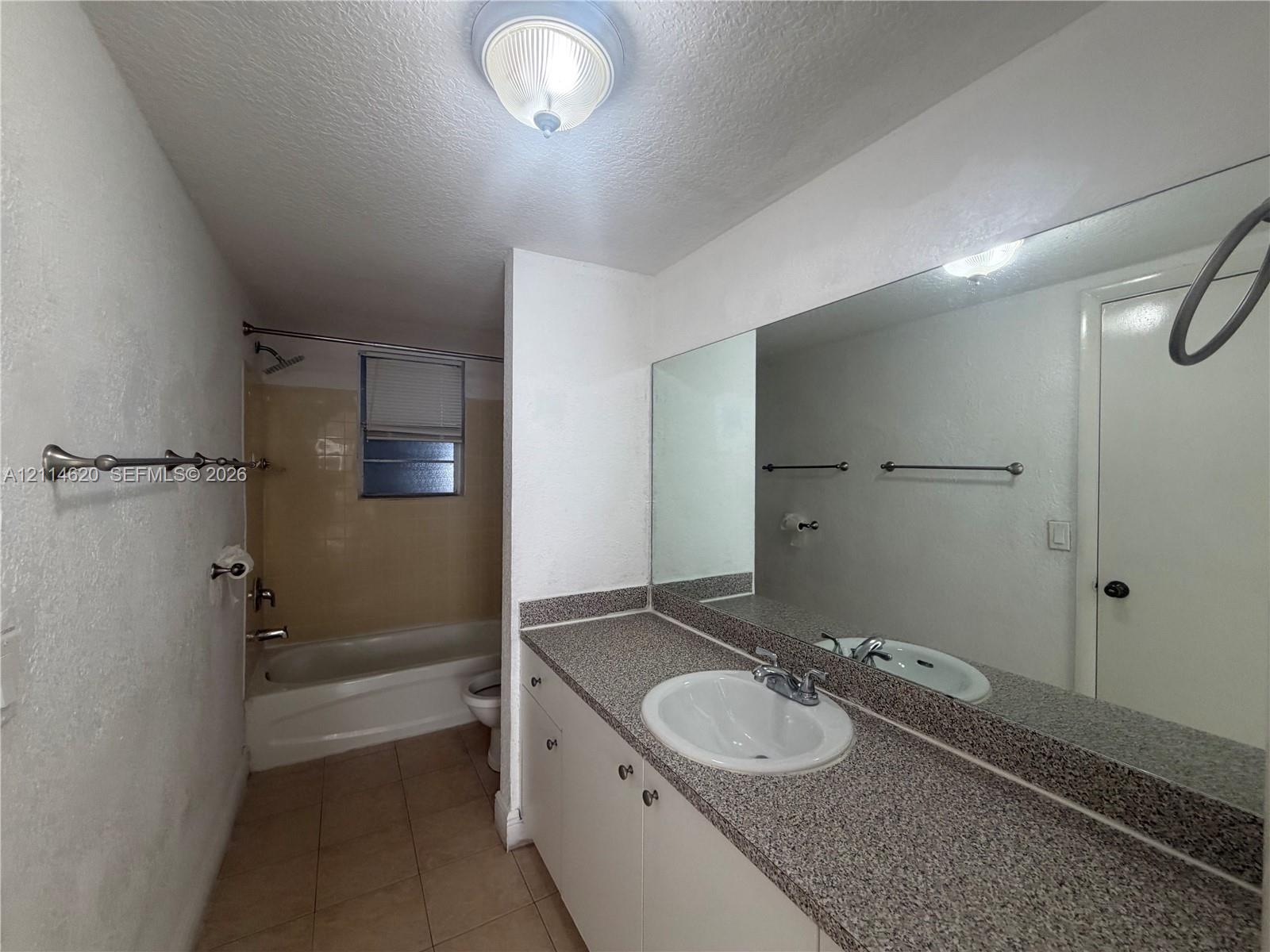 Bathroom featuring a vanity with a stone-finish countertop, integrated oval sink, full-width wall mirror, tile flooring, and a tub-shower combination with tiled surround