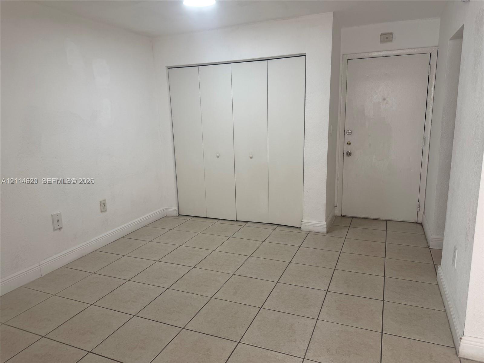 Neutral-toned ceramic tile flooring, four-panel closet with white doors, and a solid-panel entry door
