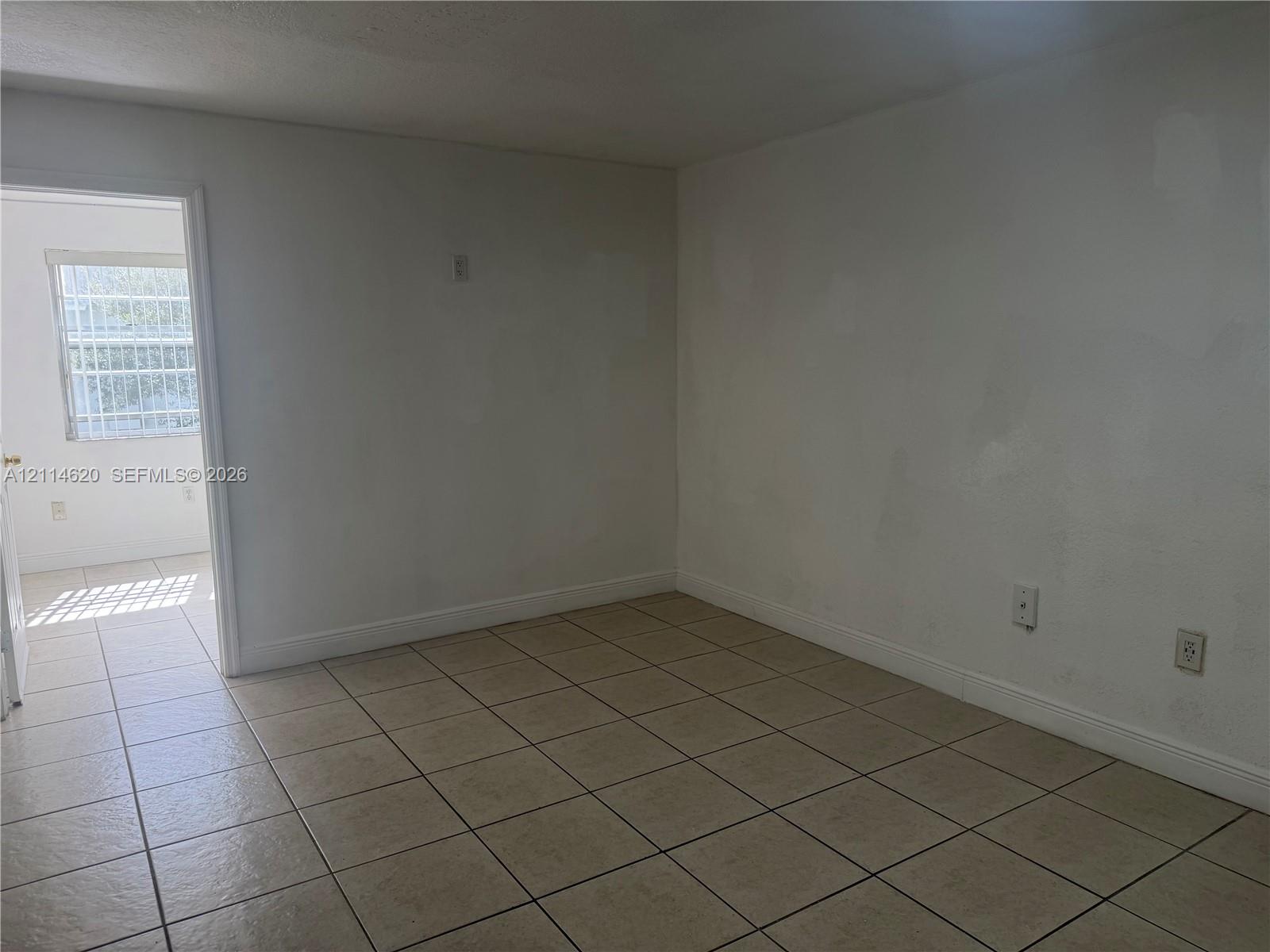 Interior space featuring neutral wall finishes, tile flooring, and a window with security bars