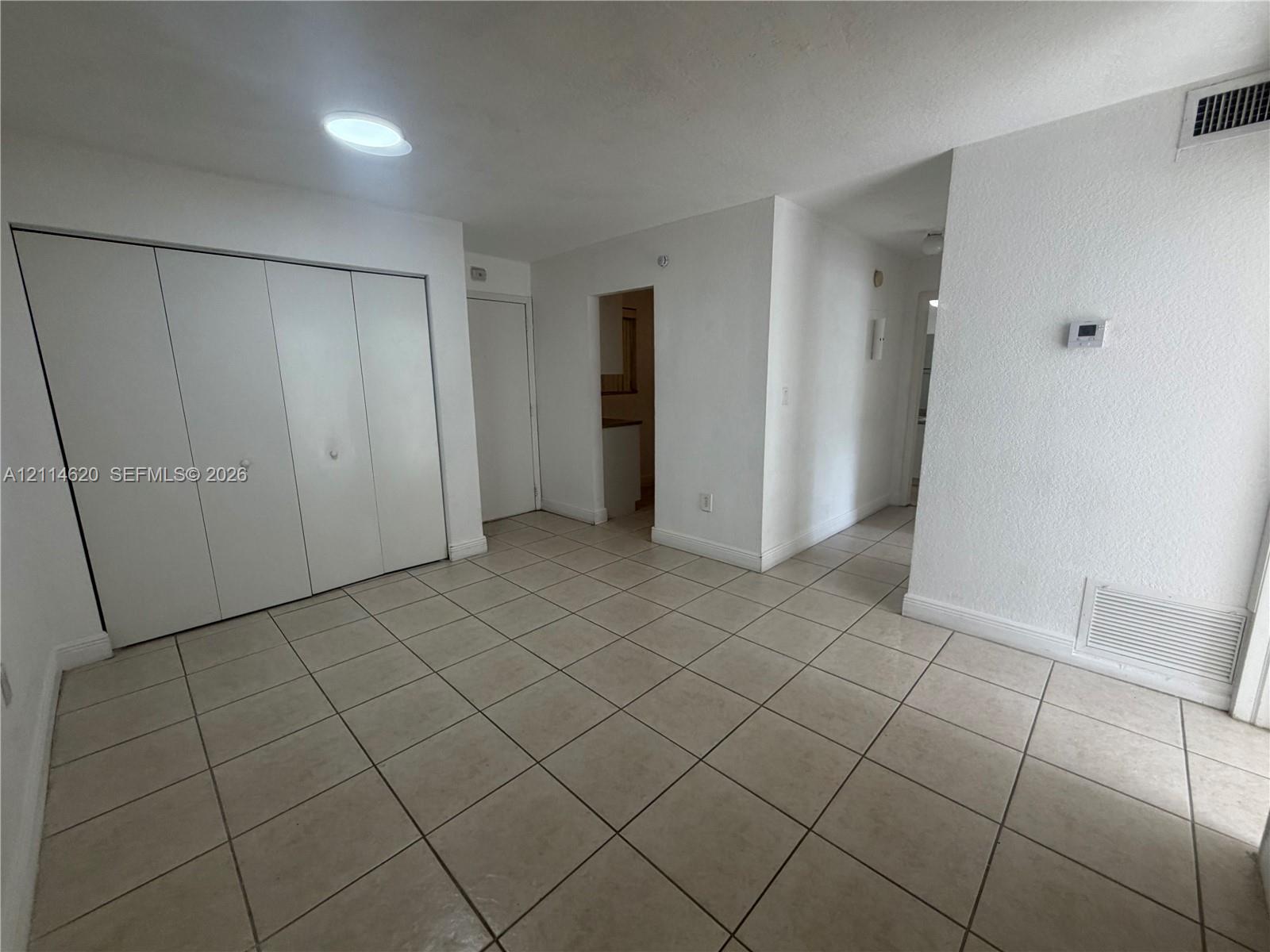 Neutral-toned ceramic tile flooring, built-in closet with multi-panel sliding doors, and ceiling-mounted flush lighting