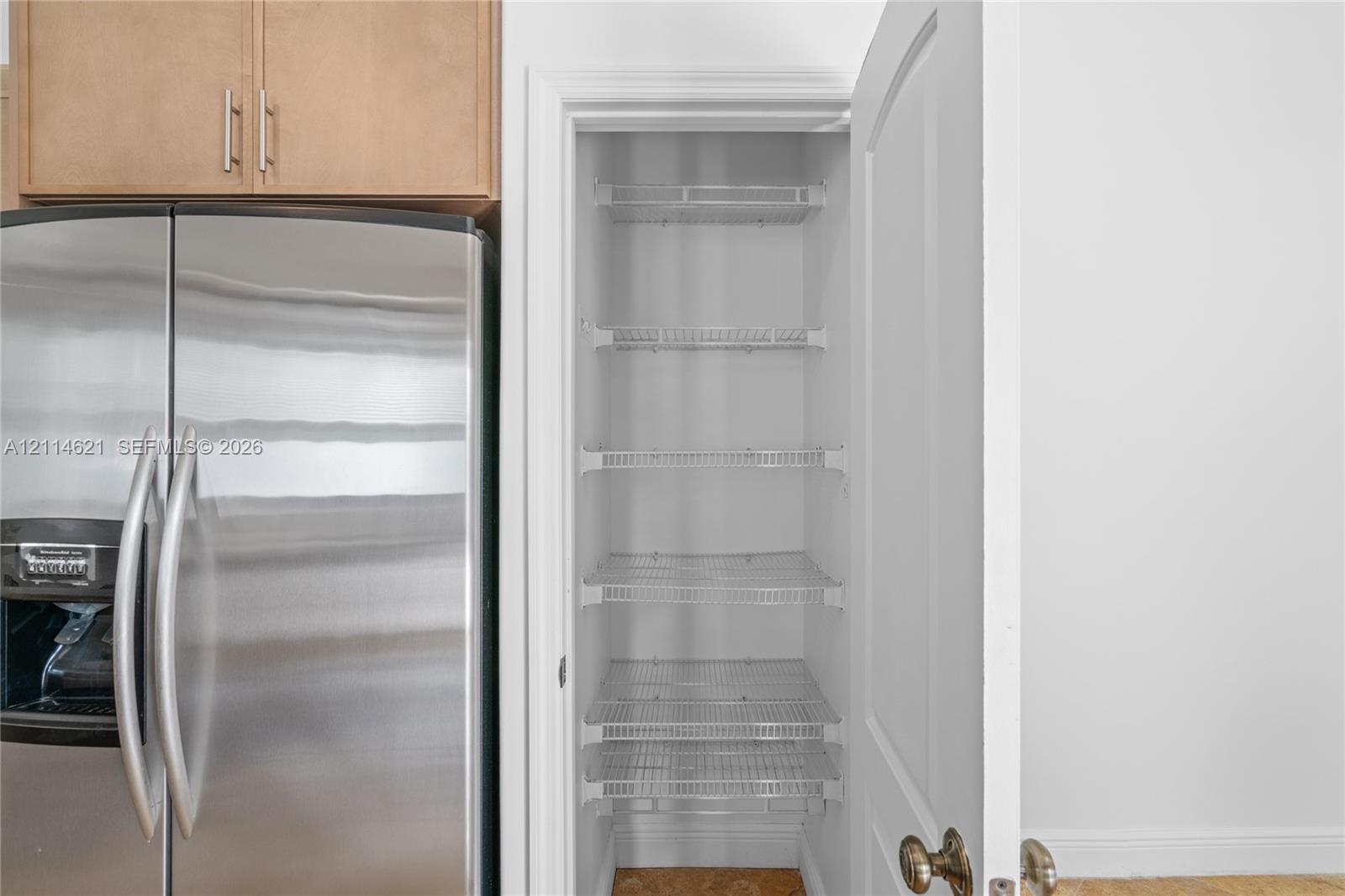 Pantry featuring multi-level wire shelving and a traditional hinged door, positioned beside stainless steel refrigeration and wood-finish cabinetry