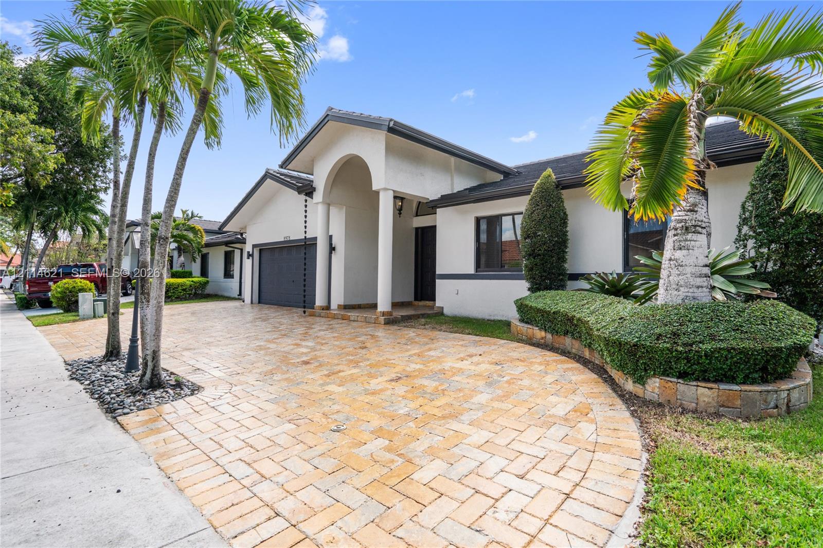 Stucco exterior featuring an arched entryway, a stone-paver driveway, and an attached multi-car garage