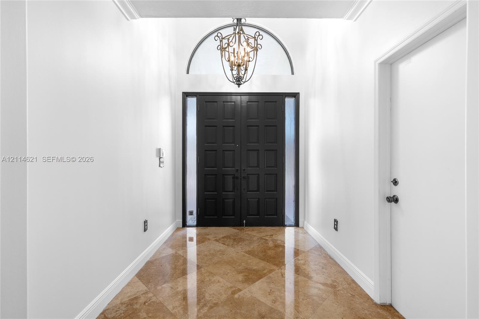 Foyer featuring double entry doors with vertical glass sidelights, an arched transom window, a multi-tiered metal chandelier, and diagonal-set stone-finish flooring