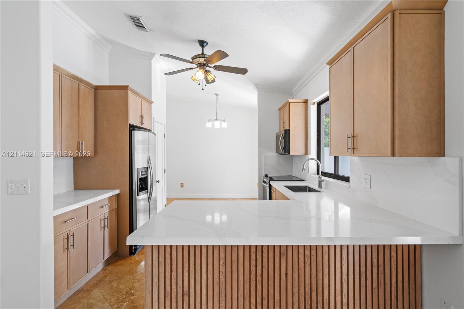 Kitchen featuring flat-panel wood cabinetry, white stone-finish countertops, slatted wood kitchen island detailing, stainless steel appliances, and a mounted ceiling fan Kitchen featuring flat-panel wood cabinetry, white stone-finish countertops, slatted wood kitchen island detailing, stainless steel appliances, and a mounted ceiling fan