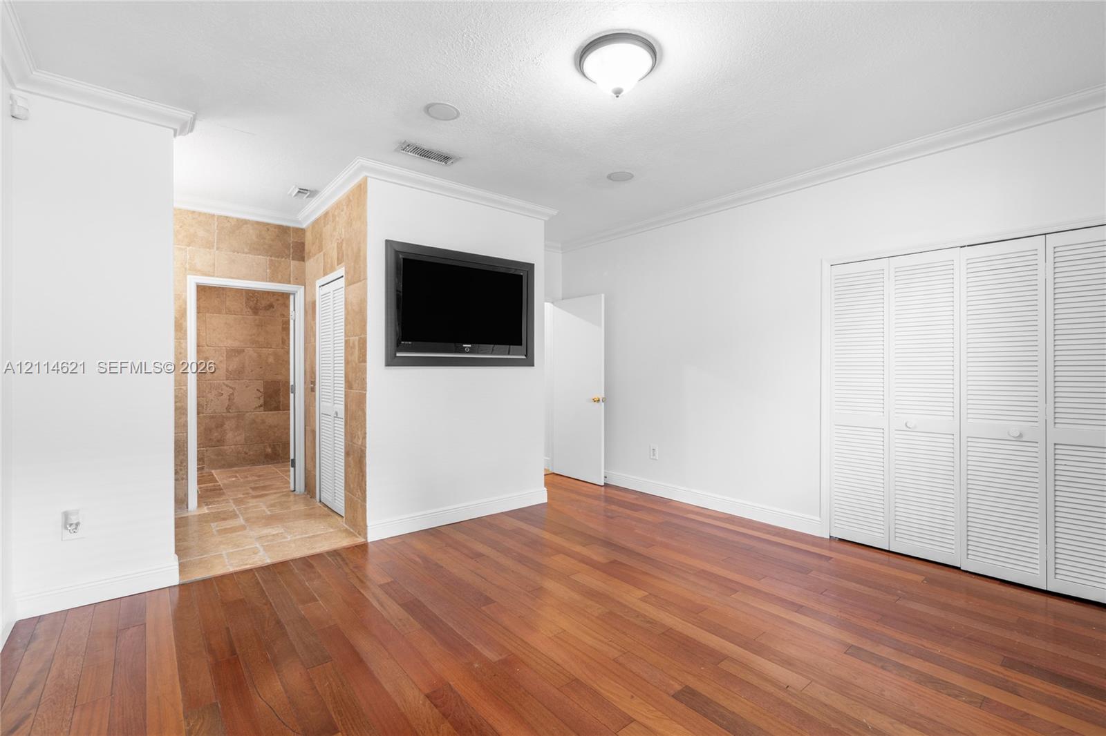 Interior space featuring wood-finish flooring, white louvered closet doors, recessed ceiling lighting, and crown molding, with stone-tile finishes visible in the recessed area