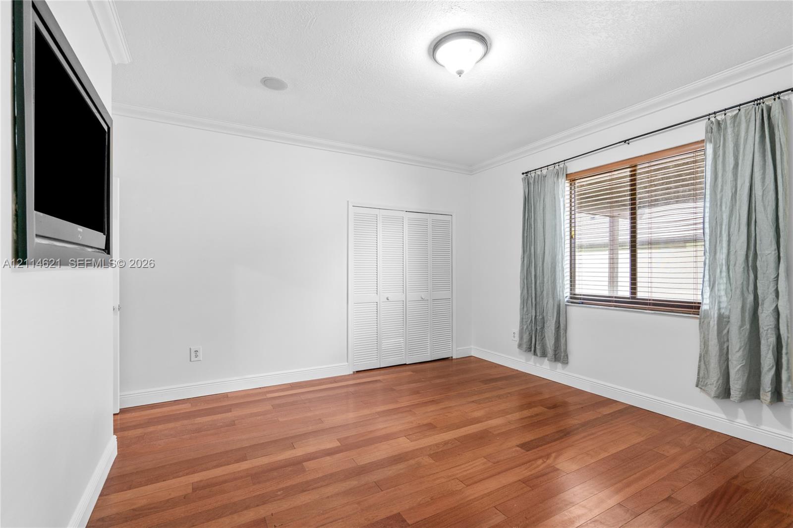 Room featuring wood-finish flooring, crown molding, a flush-mount ceiling light fixture, and a multi-panel closet with louvered doors