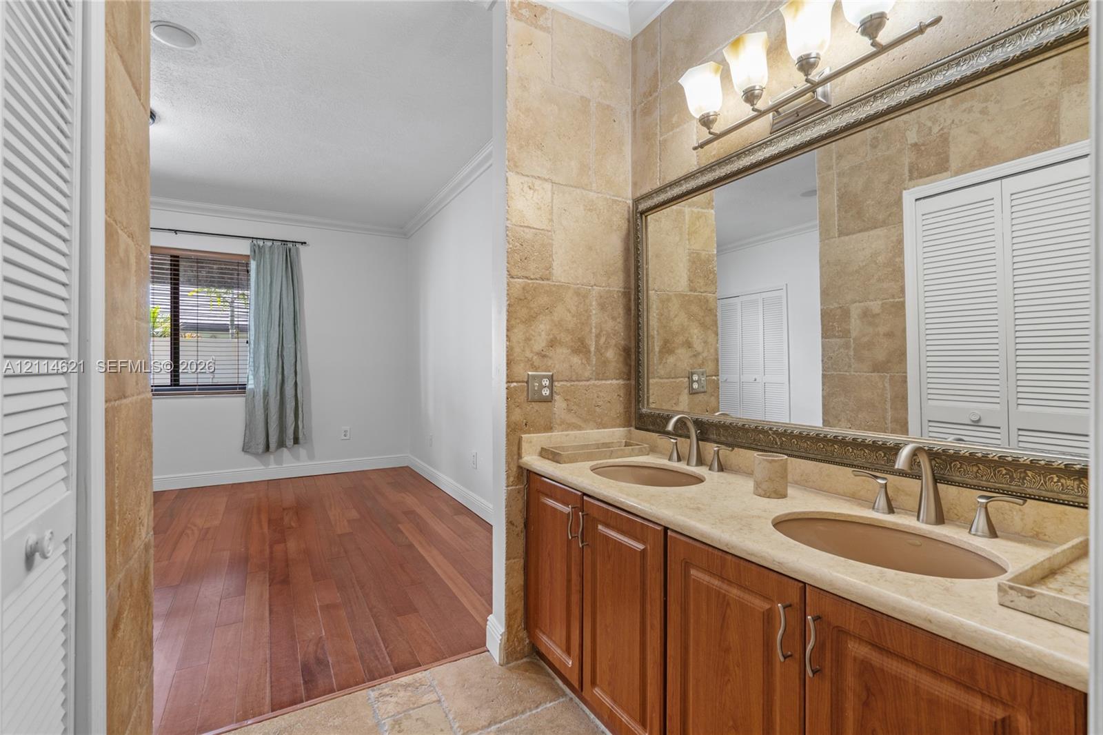 Double vanity with stone-style countertop and undermount sinks, wood-finish cabinetry, tile wall surround, and three-light decorative vanity fixture