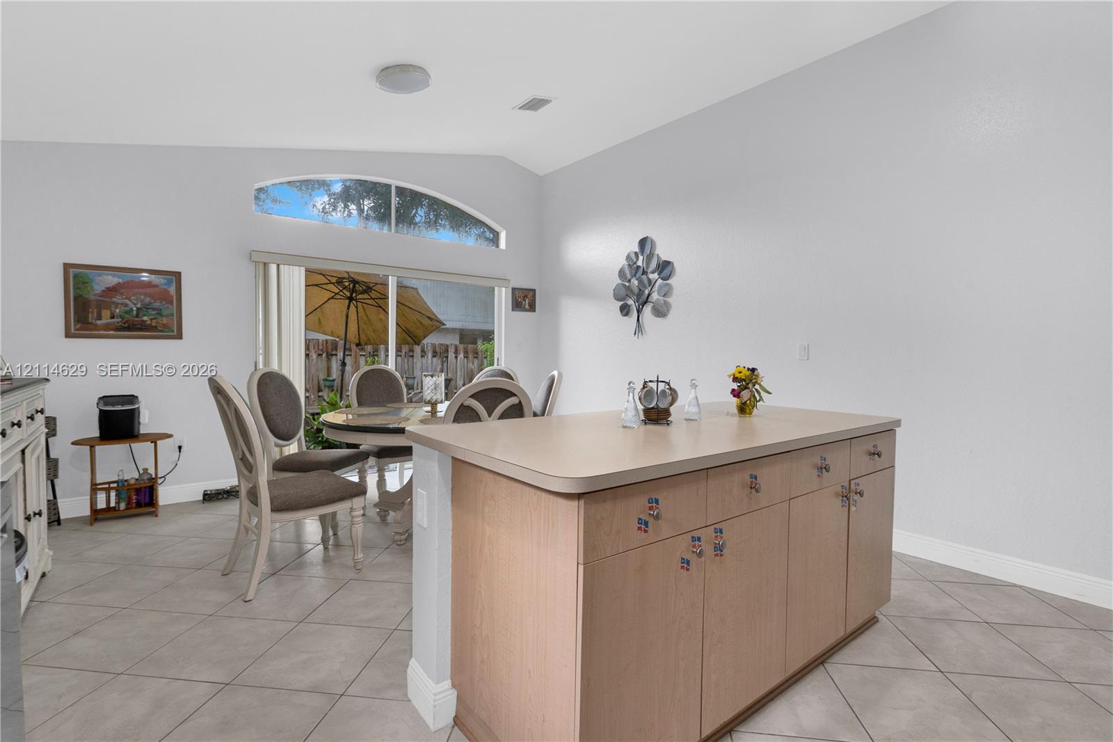 Kitchen island featuring wood-finish cabinetry and a solid-surface countertop, tile flooring, vaulted ceilings, and a sliding glass door topped with an arched window