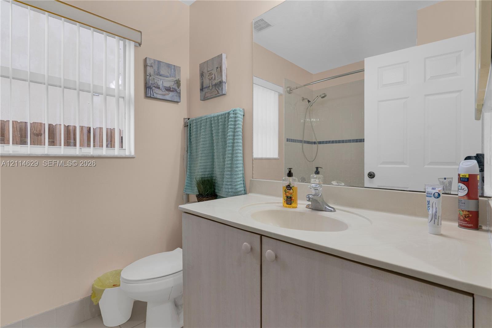 Bathroom featuring a vanity with an integrated sink and light-toned cabinetry, an expansive wall-mounted mirror, a tub-shower combination with a showerhead, and a window with horizontal blinds