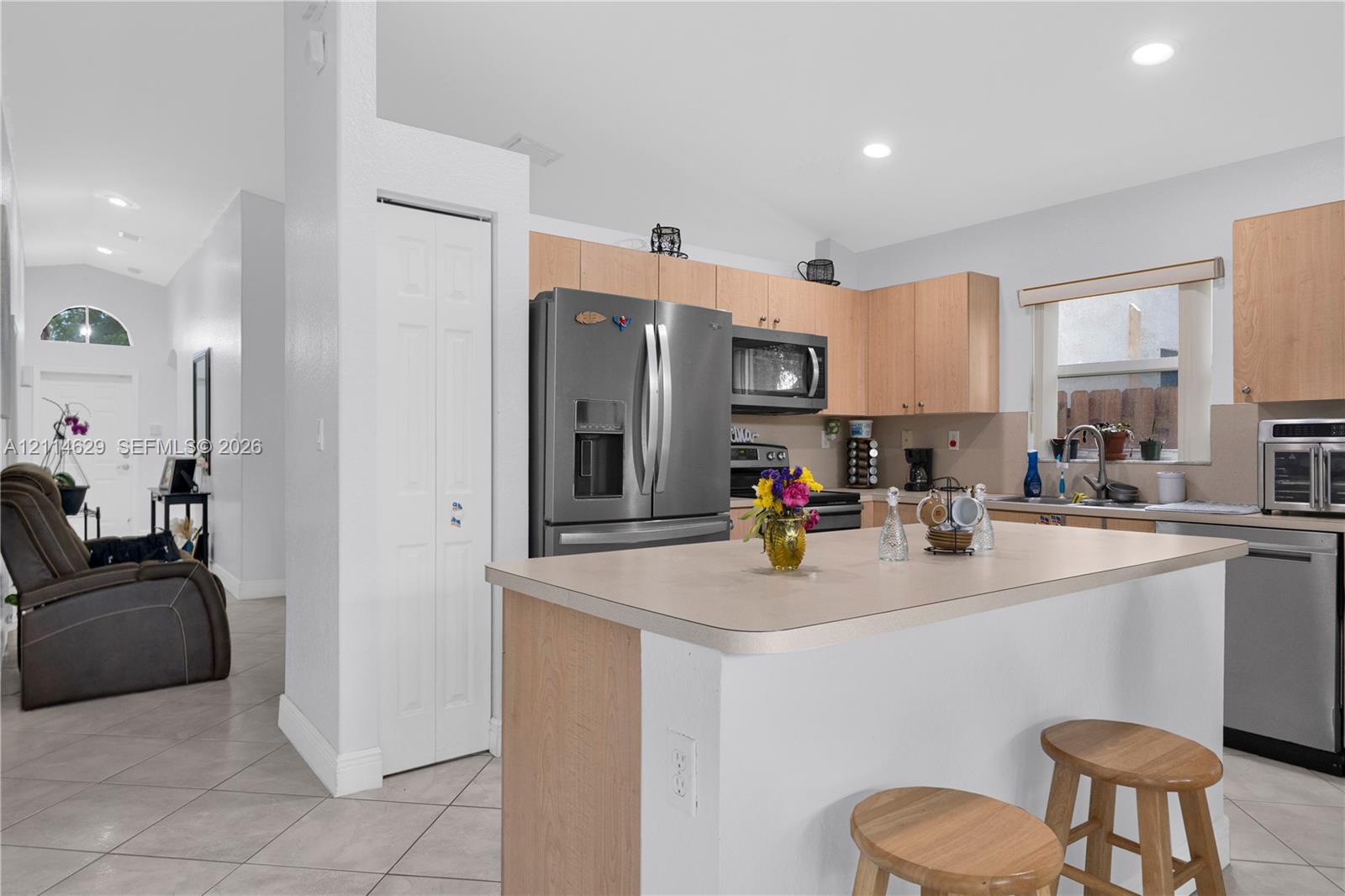Kitchen featuring light wood cabinetry, stainless steel appliances, a center island with a laminate countertop, and neutral tile flooring