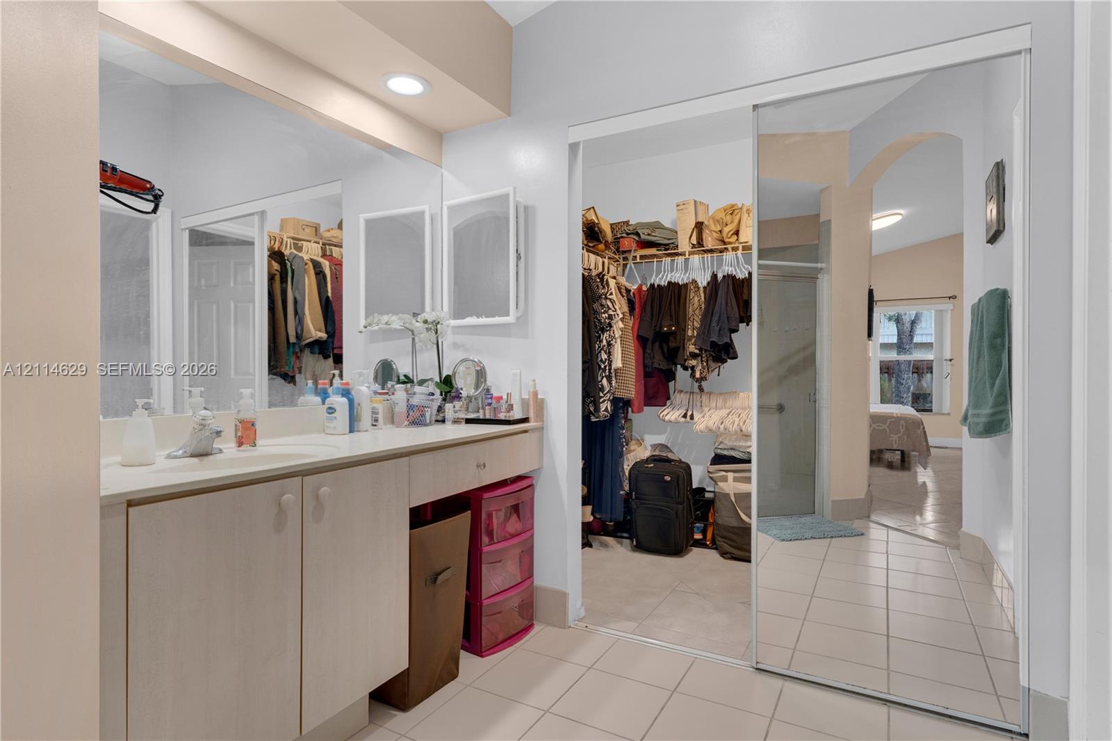 Vanity featuring neutral cabinetry and a solid surface countertop with a single-basin sink, accompanied by a large wall-to-wall mirror, recessed lighting, and mirrored sliding closet doors