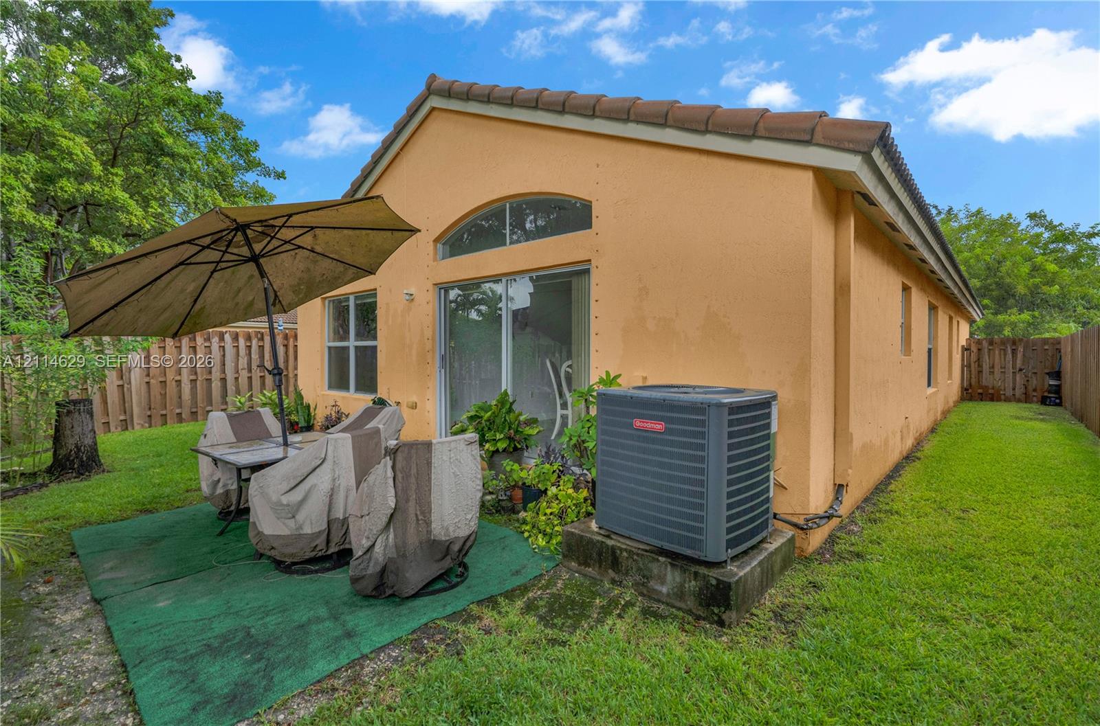 Rear exterior featuring stucco siding, a tiled roof, an arched transom window, sliding glass door, and a grass-covered backyard enclosed by a wood fence
