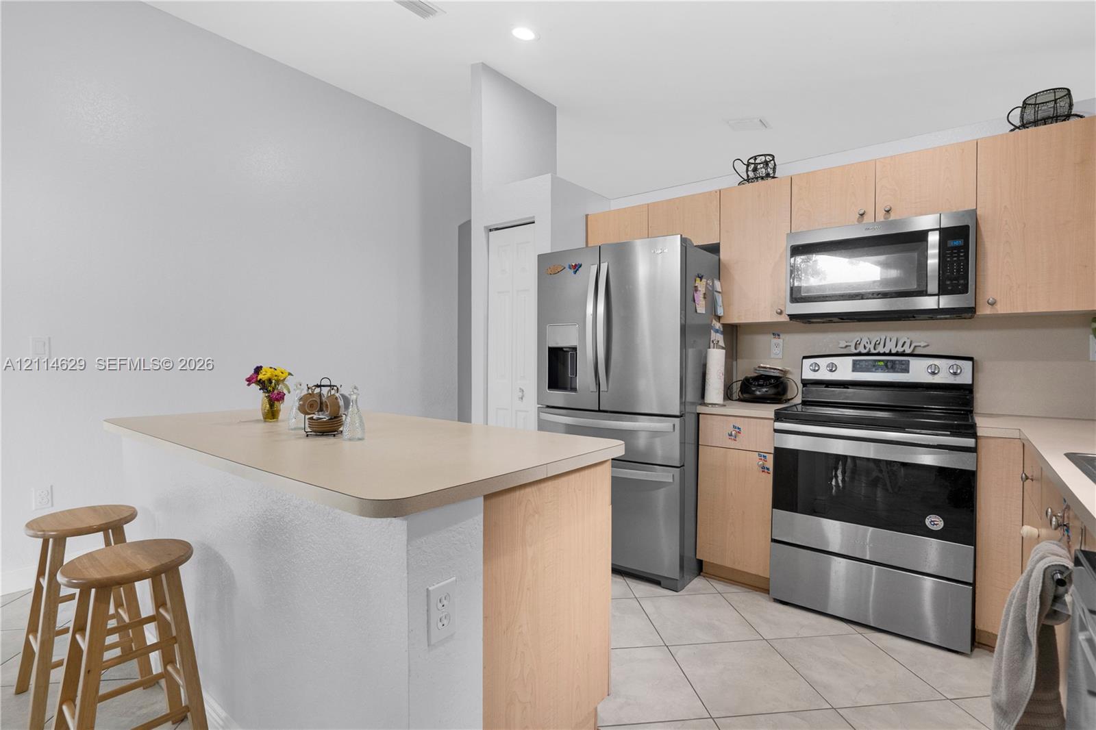 Kitchen featuring wood-finish cabinetry, a central island with a countertop, stainless steel appliances, and tile flooring