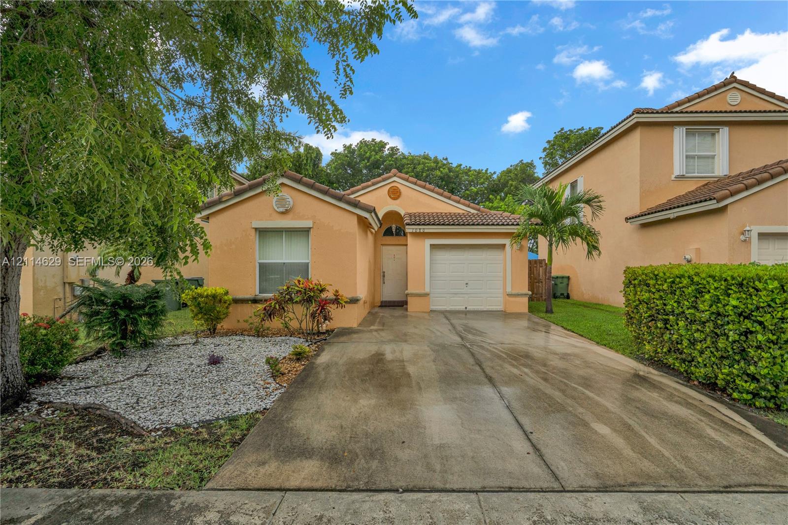 Single-story exterior featuring a stucco facade, tile roof, attached one-car garage, concrete driveway, and rock landscaping