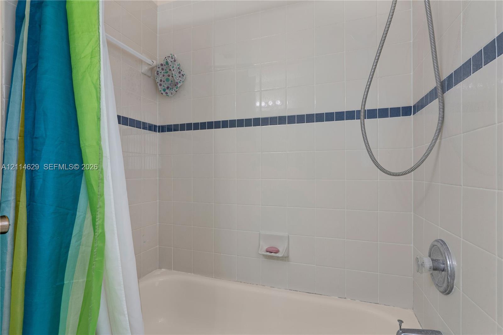 Bathtub enclosure featuring white square wall tile, blue accent tile trim, integrated soap dish, and a handheld shower fixture