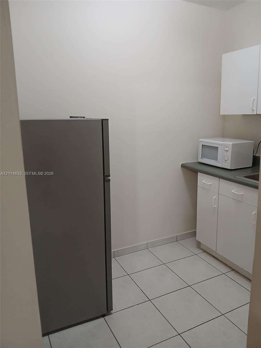 Stainless steel refrigerator, white cabinetry, solid-surface countertops, and tiled flooring