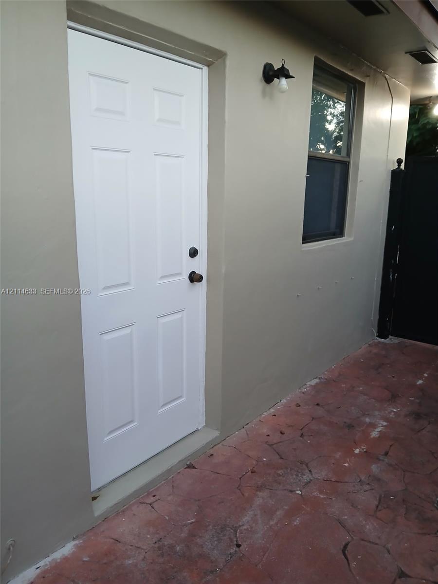 Exterior entrance featuring a six-panel door, stone-patterned concrete paving, and a wall-mounted outdoor light fixture