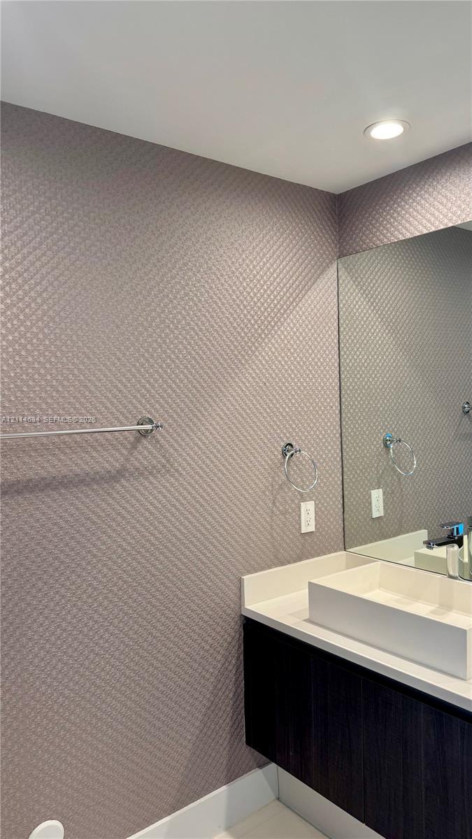 Wall-mounted vanity with a rectangular vessel sink, solid-surface countertop, recessed ceiling lighting, and textured wall finish