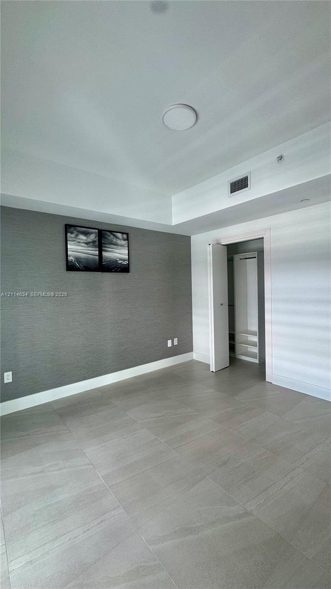 Neutral-toned tile flooring, accent wall with textured finish, recessed ceiling lighting, and built-in closet storage