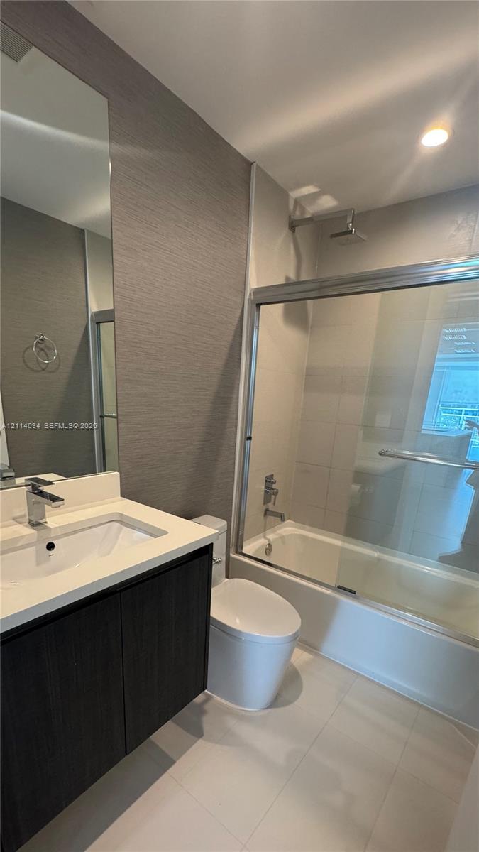 Dark wood-finish vanity with a white countertop and rectangular undermount sink, accompanied by a tub-shower combination featuring a sliding glass enclosure and a rainfall showerhead